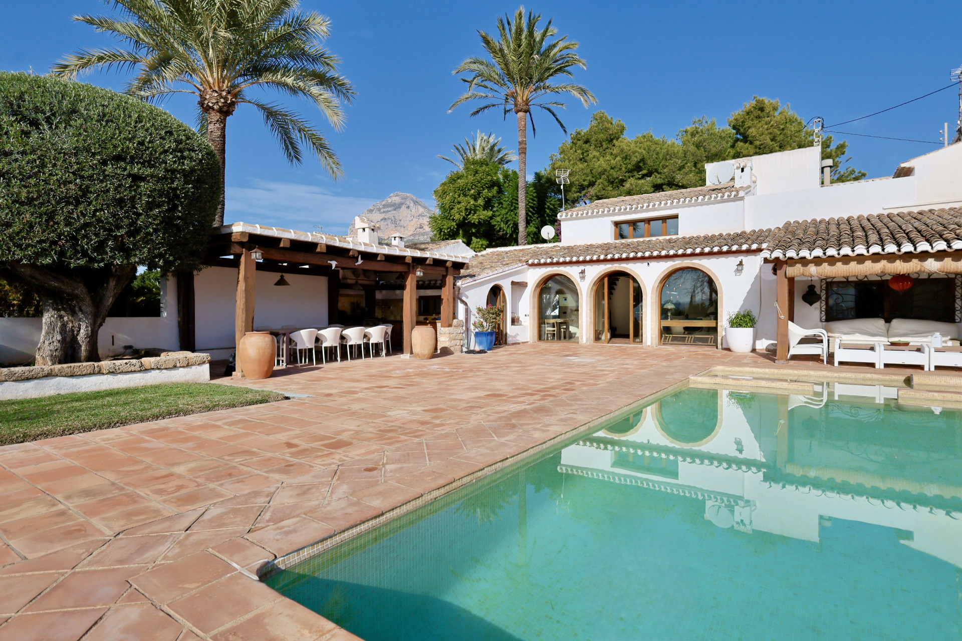 Poolblick mit Terrakottafliesen, überdachte Terrasse mit Sitzgelegenheiten und Villa-Bögen.