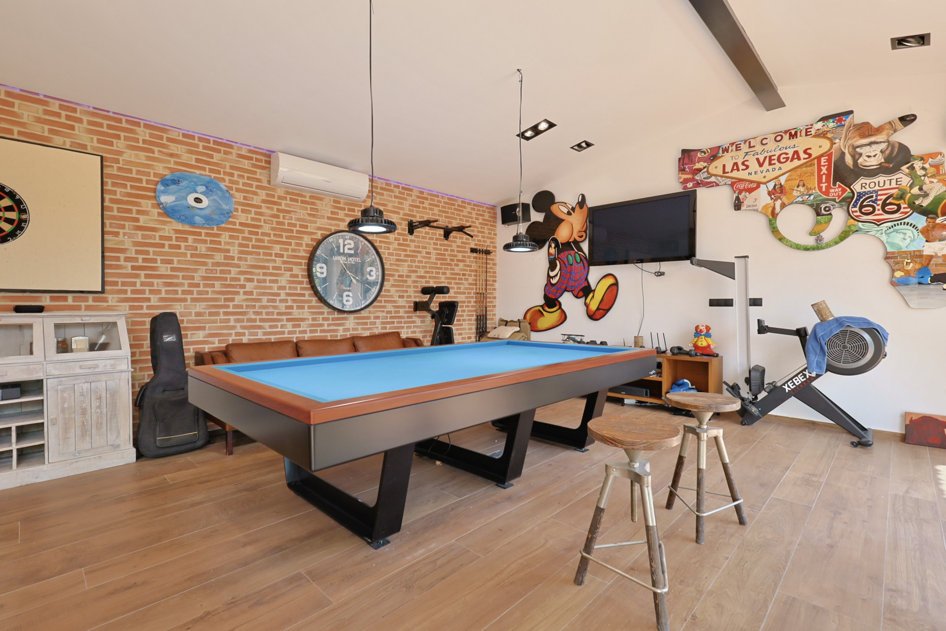Spielzimmer mit blauem Billardtisch, Backsteinwand und thematischer Dekoration.