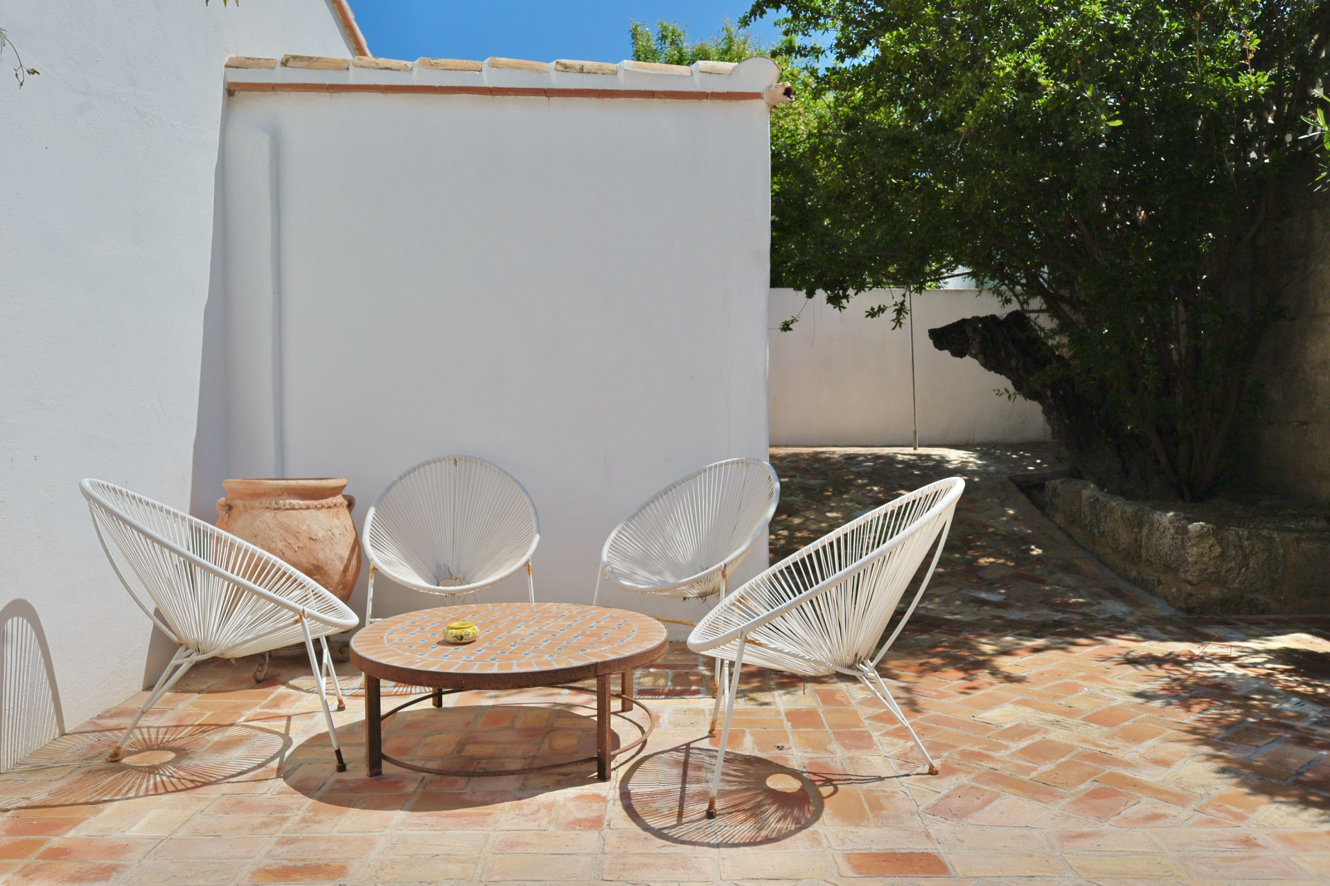 Terrasse mit Terrakottaboden, weißen Schnurstühlen und Mosaiktisch, ideal zum Entspannen im Freien.