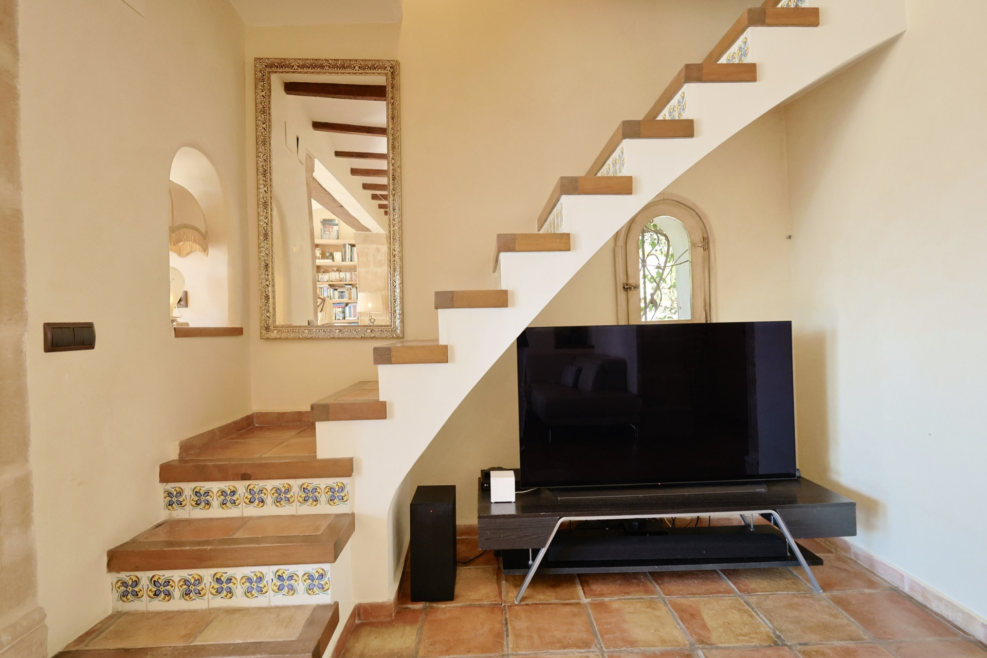 Treppendetail mit dekorativen Fliesen und TV im Wohnzimmer mit Terrakottaboden.