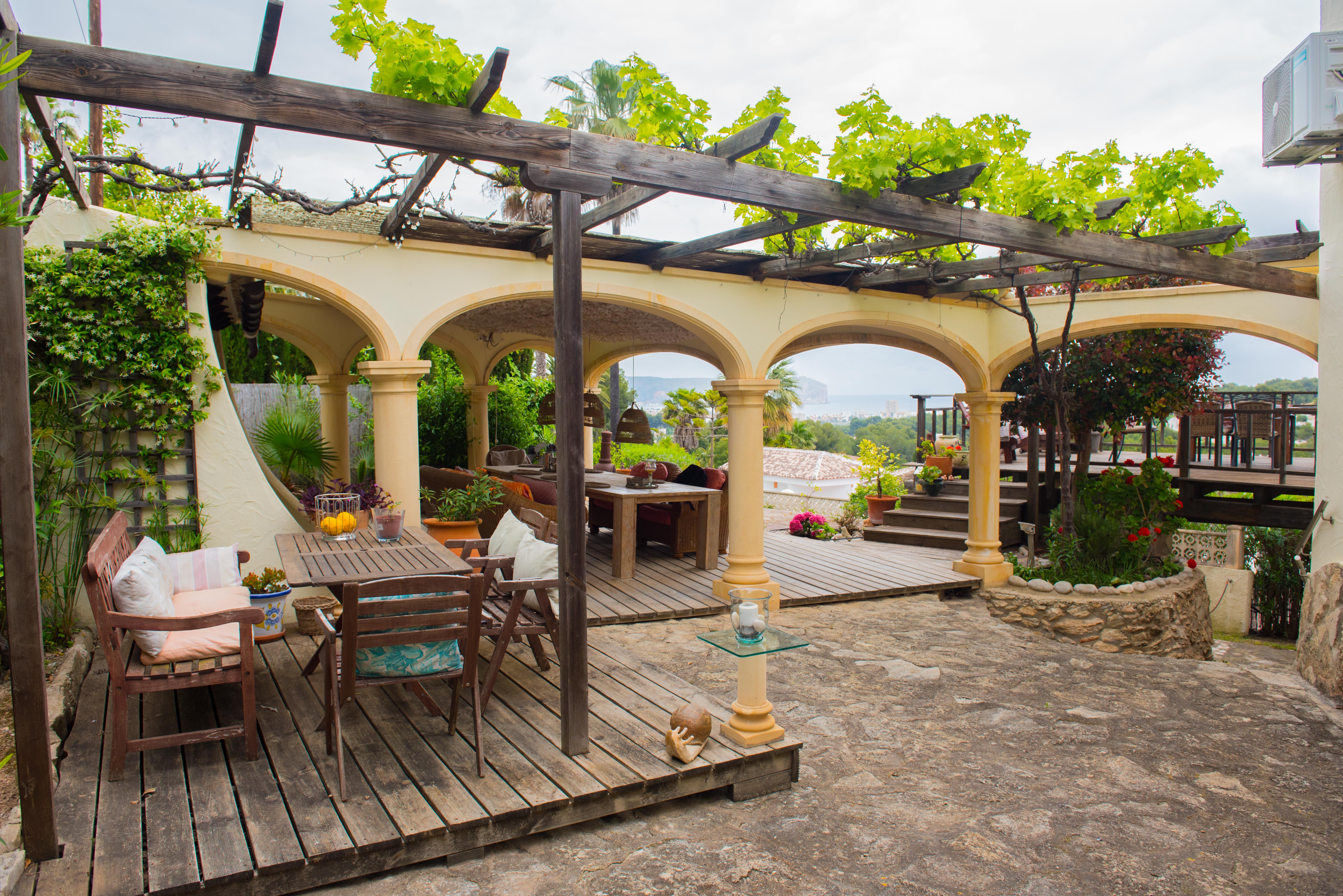 Außen-Terrasse mit Holzpergola und Weinreben, Holzdeck und ein Bogengang mit weitem Blick auf das Meer und die Küstenlandschaft.