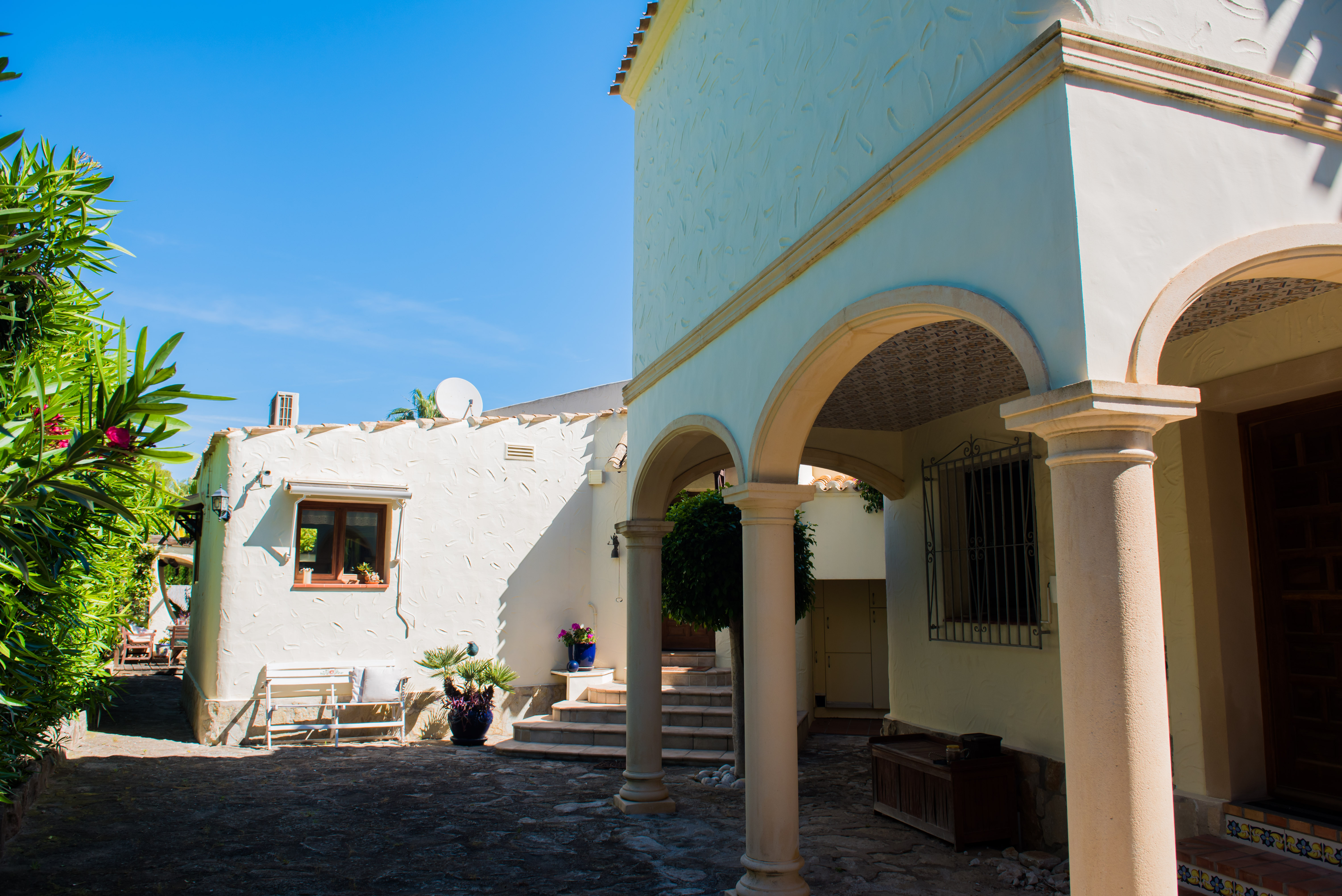Außenansicht der Villa mit Steinbögen und weißen, strukturierten Wänden, umgeben von mediterranem Grün.