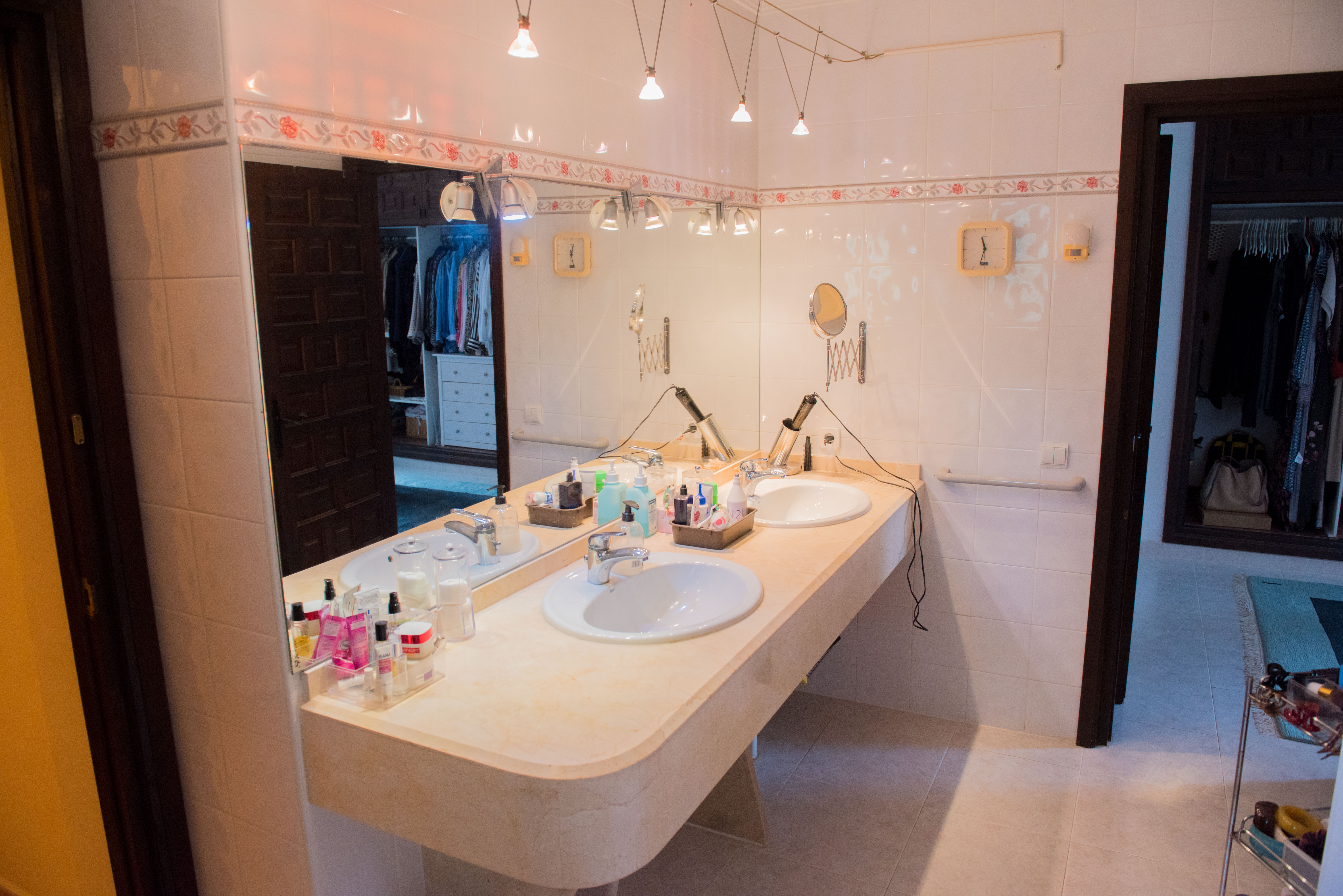Badezimmer mit Doppelwaschbecken auf einer cremefarbenen Marmorplatte, großem Spiegel und Blick in den angrenzenden begehbaren Kleiderschrank.