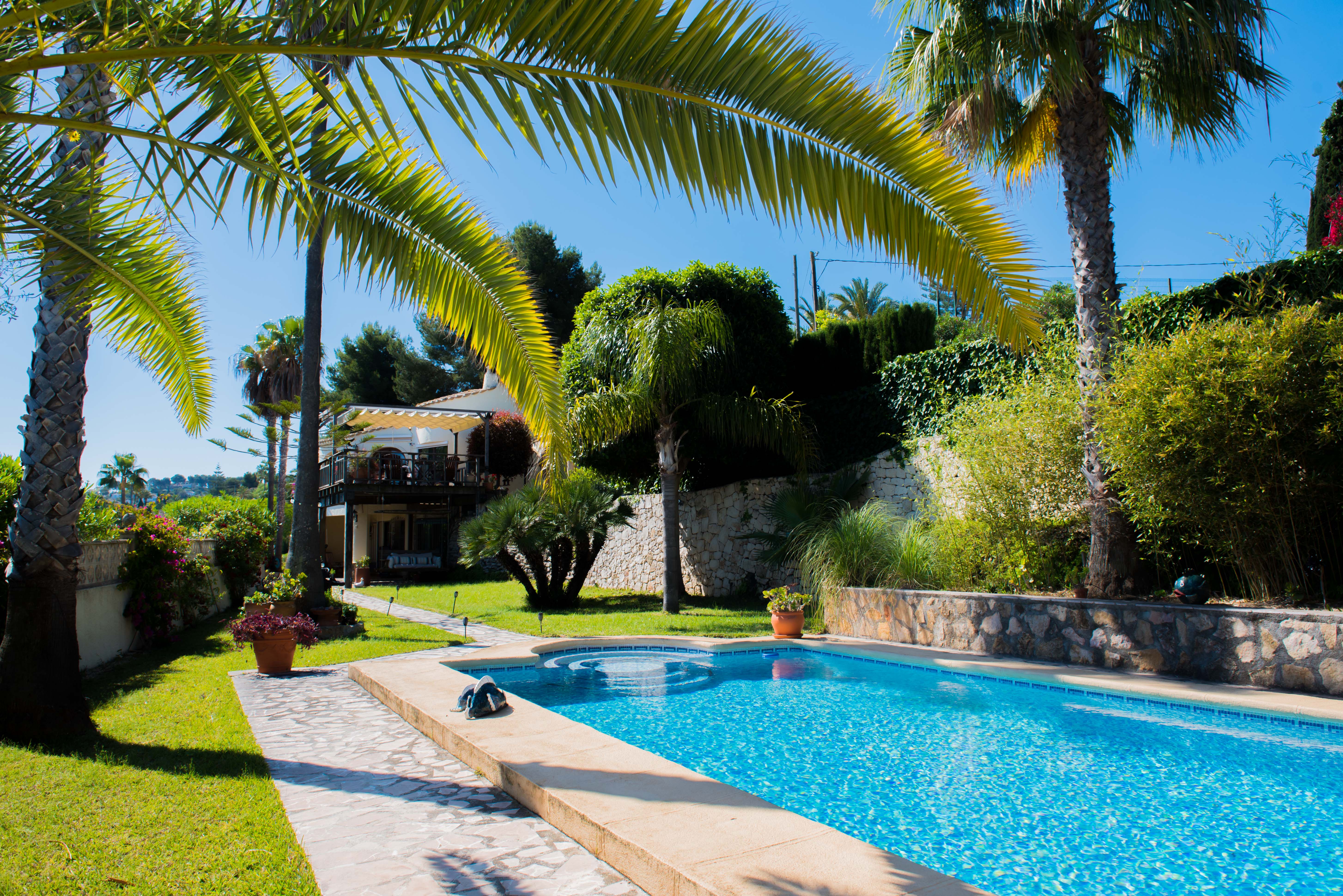 Blick auf den blau gefliesten Pool und den mediterranen Garten mit Palmen in Jávea.