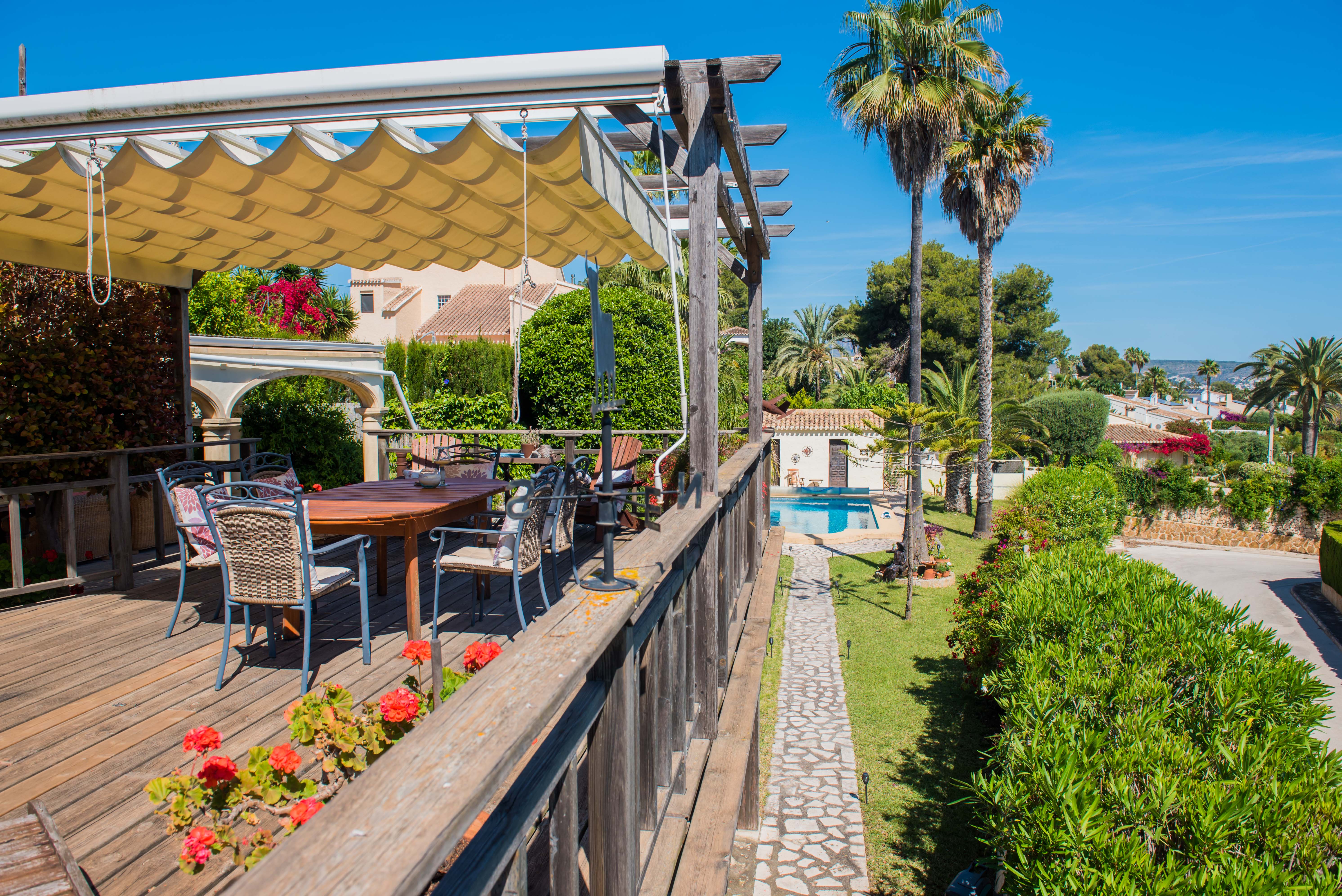 Blick von der Holzterrasse mit Markise, Tisch und Stühlen zum Pool und den Gärten.