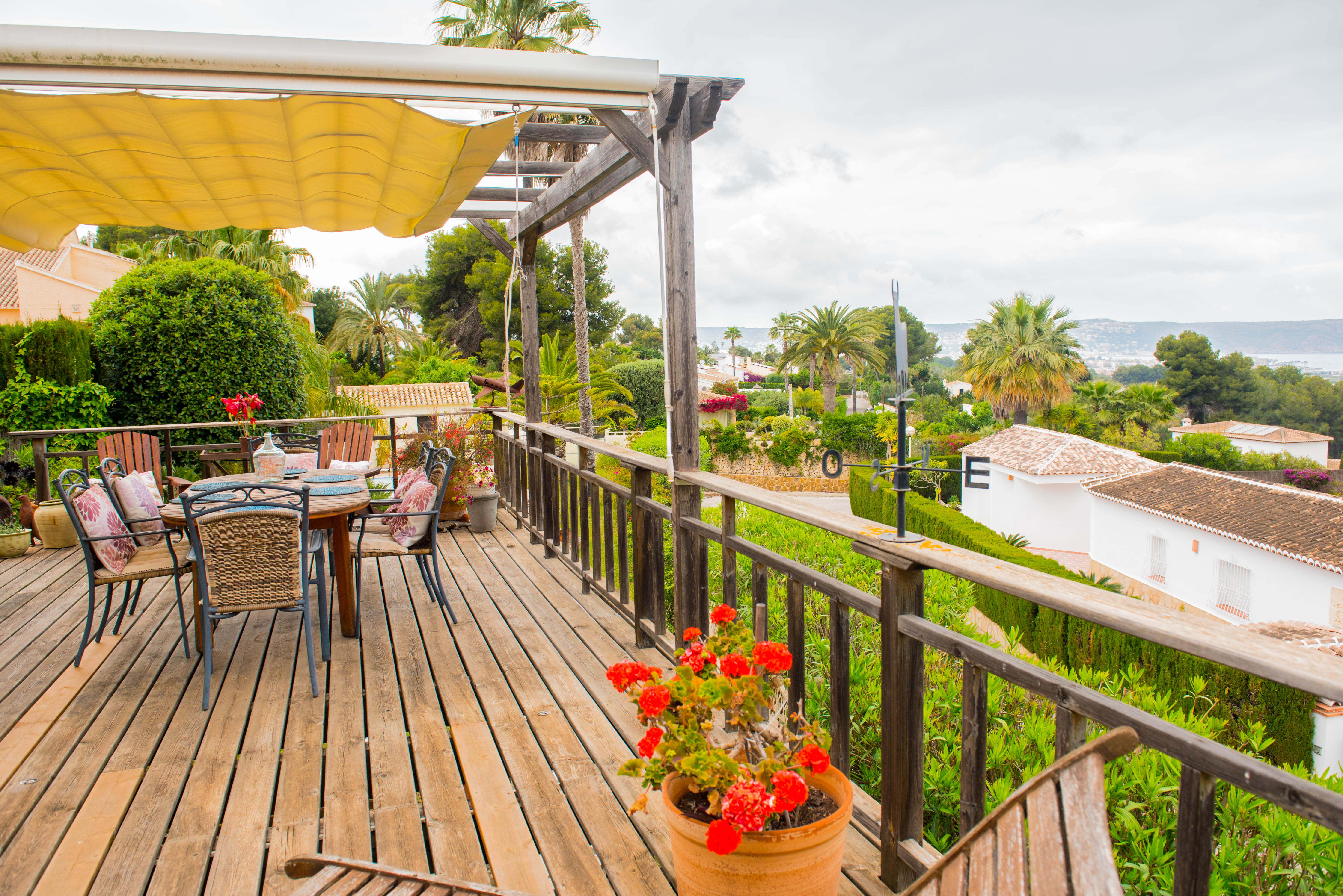 Erhöhte Holzterrasse mit ausziehbarer Markise, Essbereich im Freien und rustikalem Geländer mit Panoramablick auf das Meer und die Umgebung.