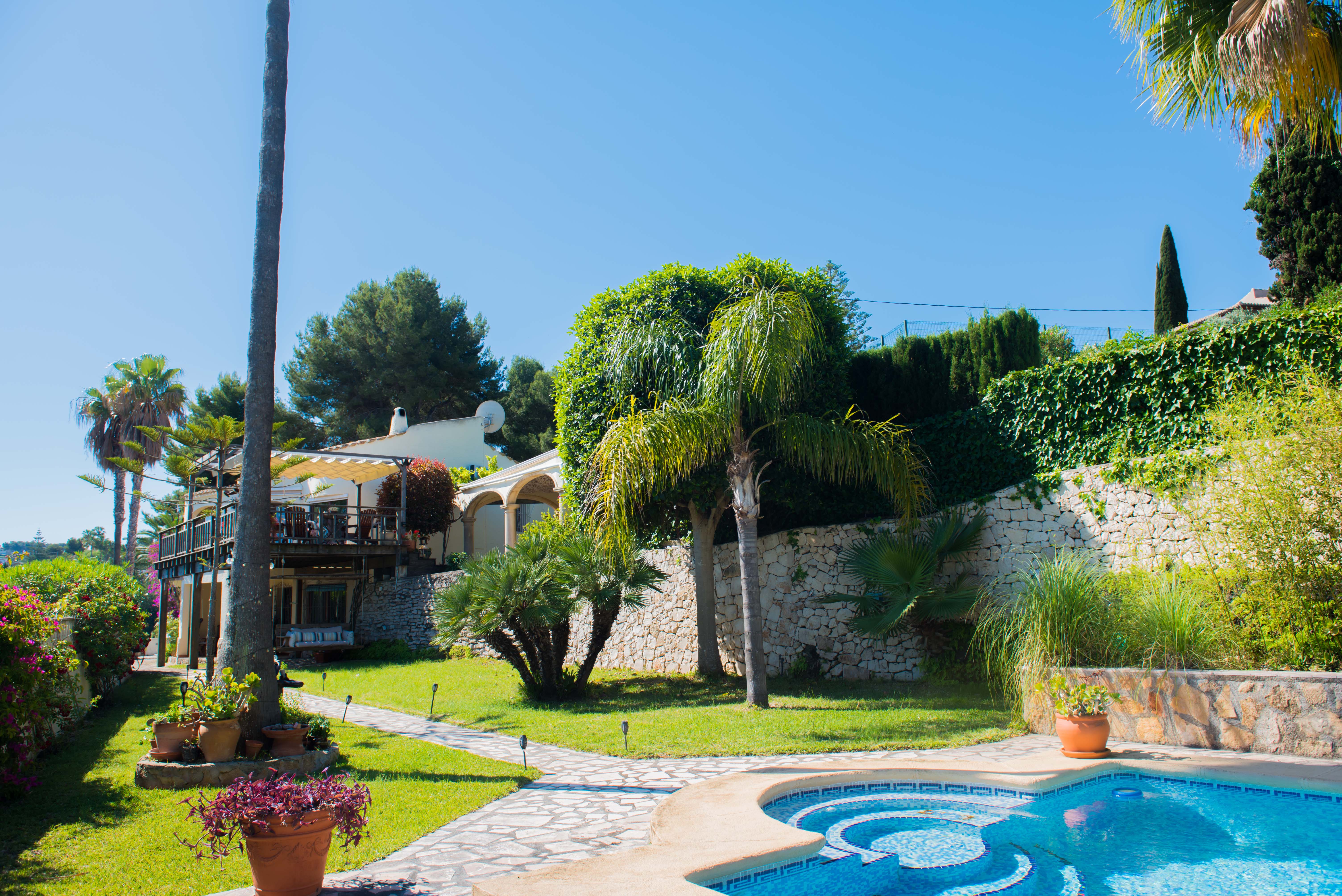 Gartenansicht mit blauem Mosaikpool und Steinpfad, der zur Villa im mediterranen Stil führt.