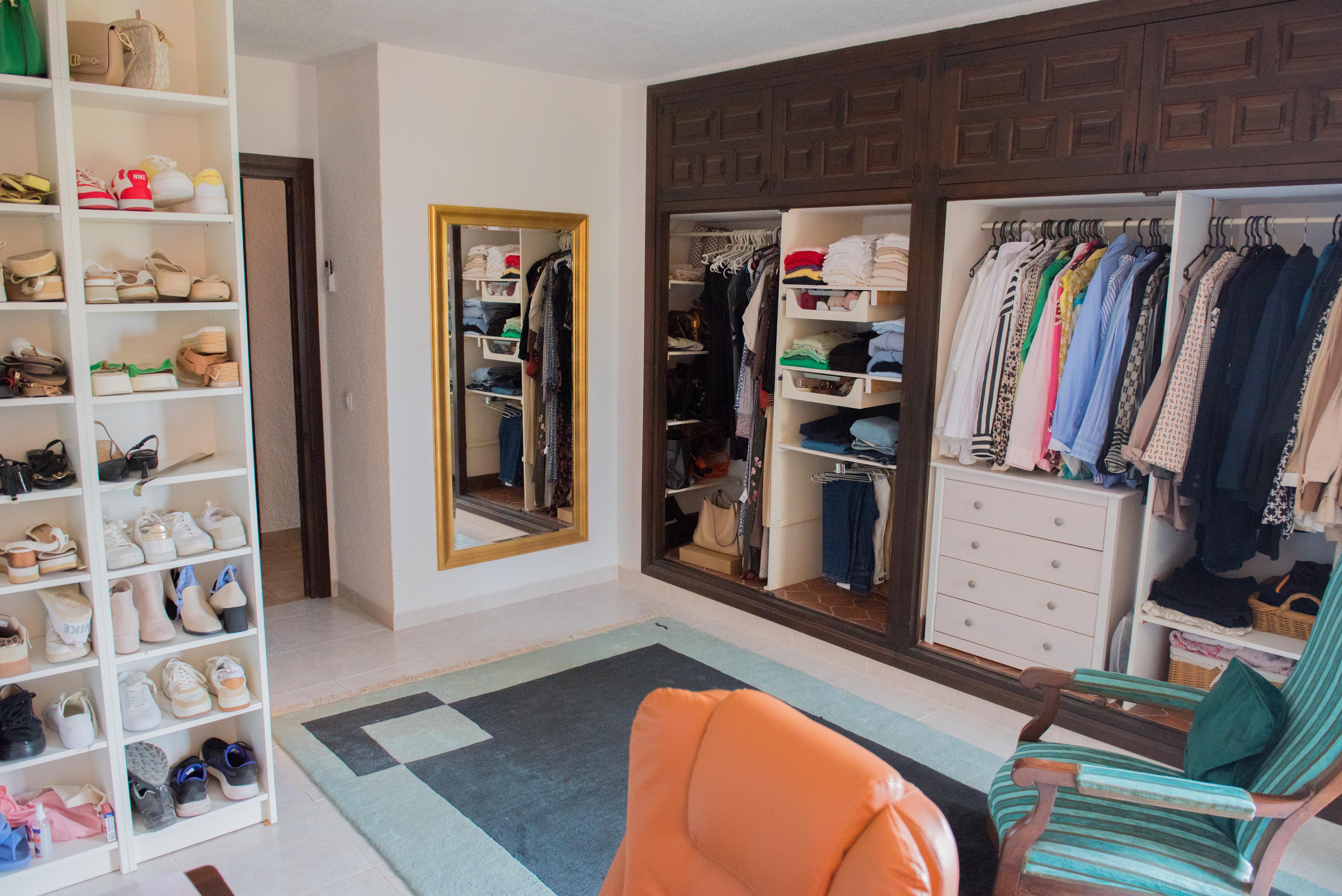 Großzügiges Ankleidezimmer mit Einbauschränken aus dunklem Holz, weißen Schuhregalen, einem Ganzkörperspiegel mit Goldrahmen und einem Sitzbereich mit geometrischem Teppich.