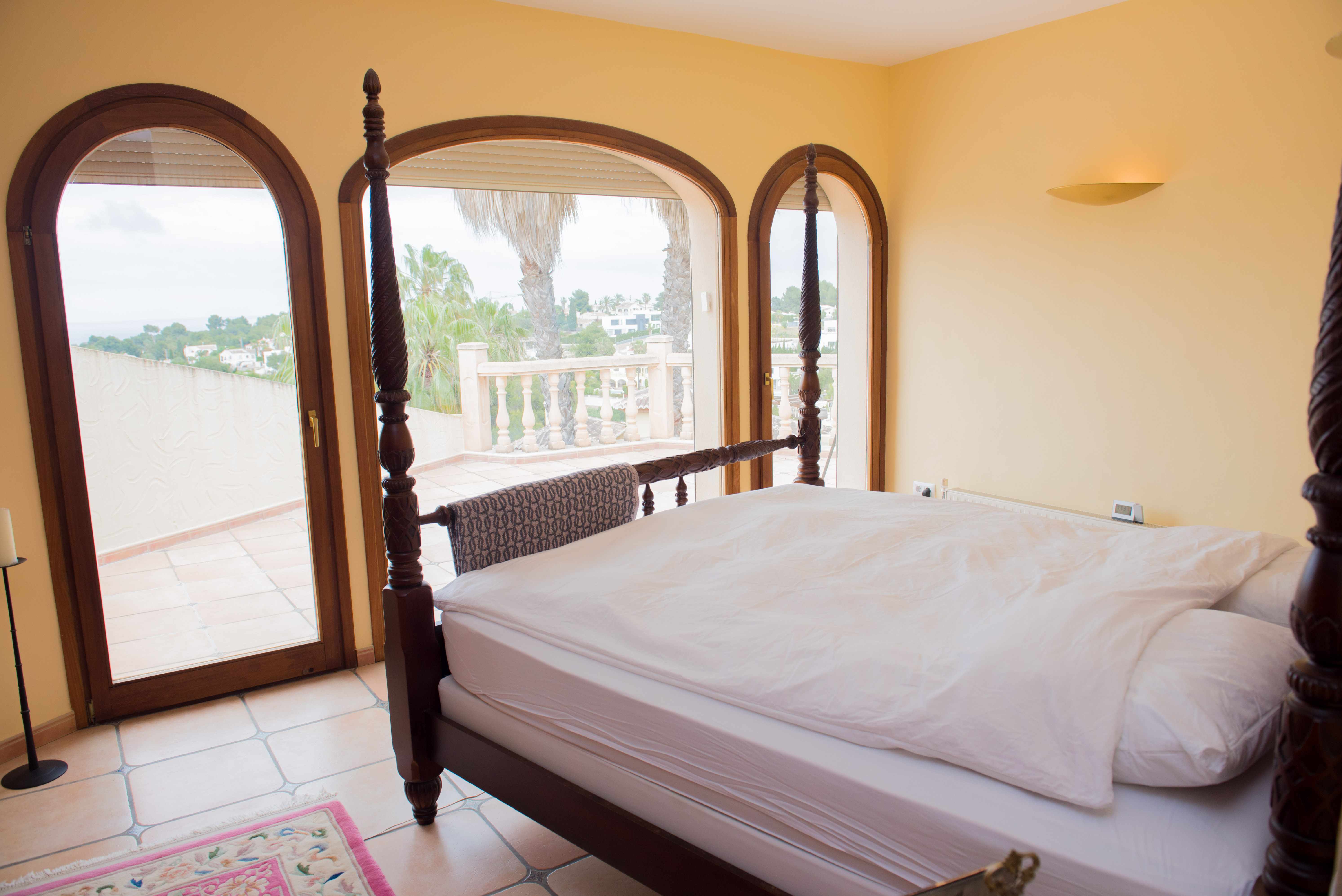 Hauptschlafzimmer mit dunklem Himmelbett aus Holz und bogenförmigen Fenstertüren, die auf die Terrasse mit Blick auf die Umgebung führen.