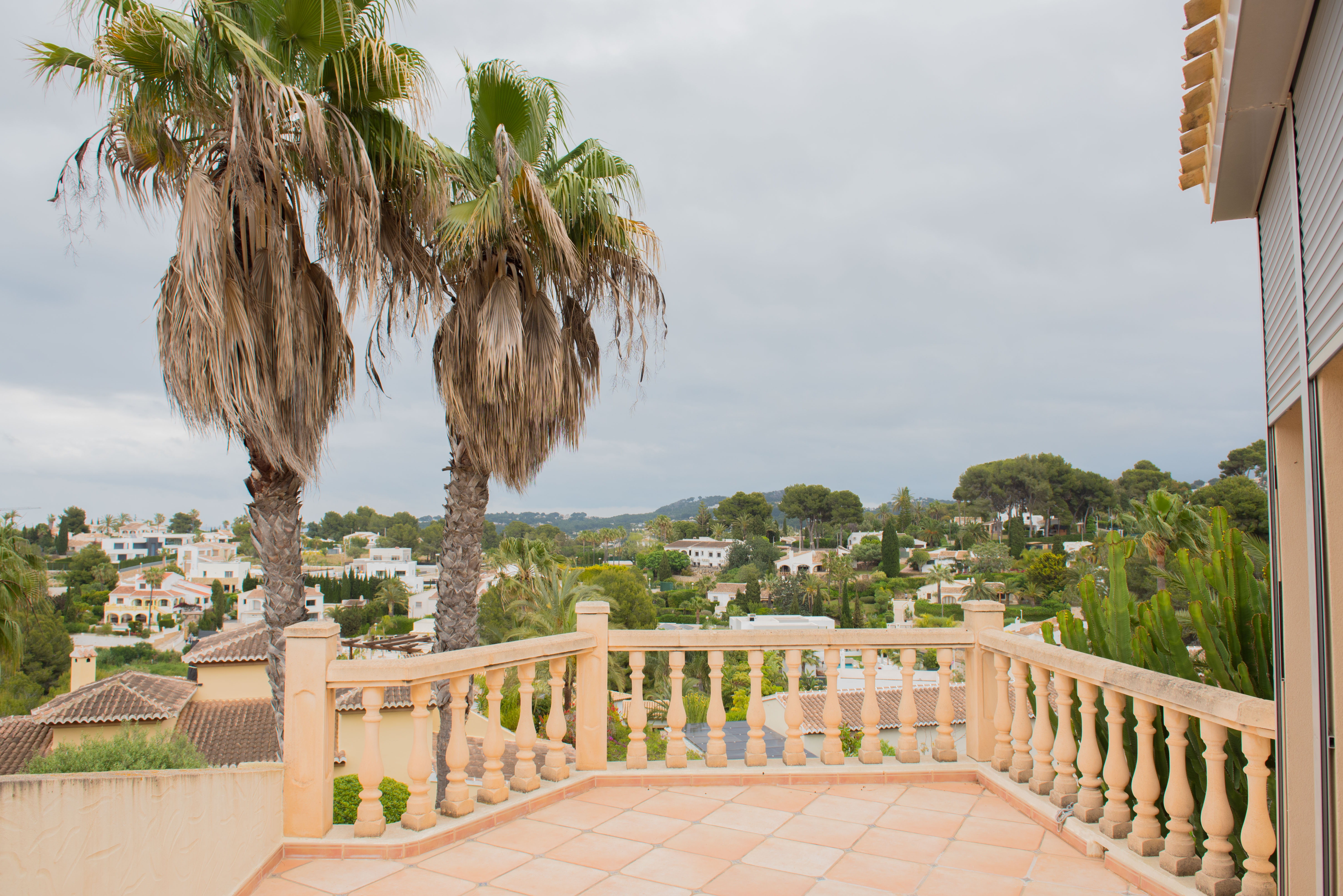 Hochgelegene Terrasse mit klassischer Steinbalustrade und Terrakottaboden, die einen Panoramablick auf die Wohngegend und Palmen bietet.