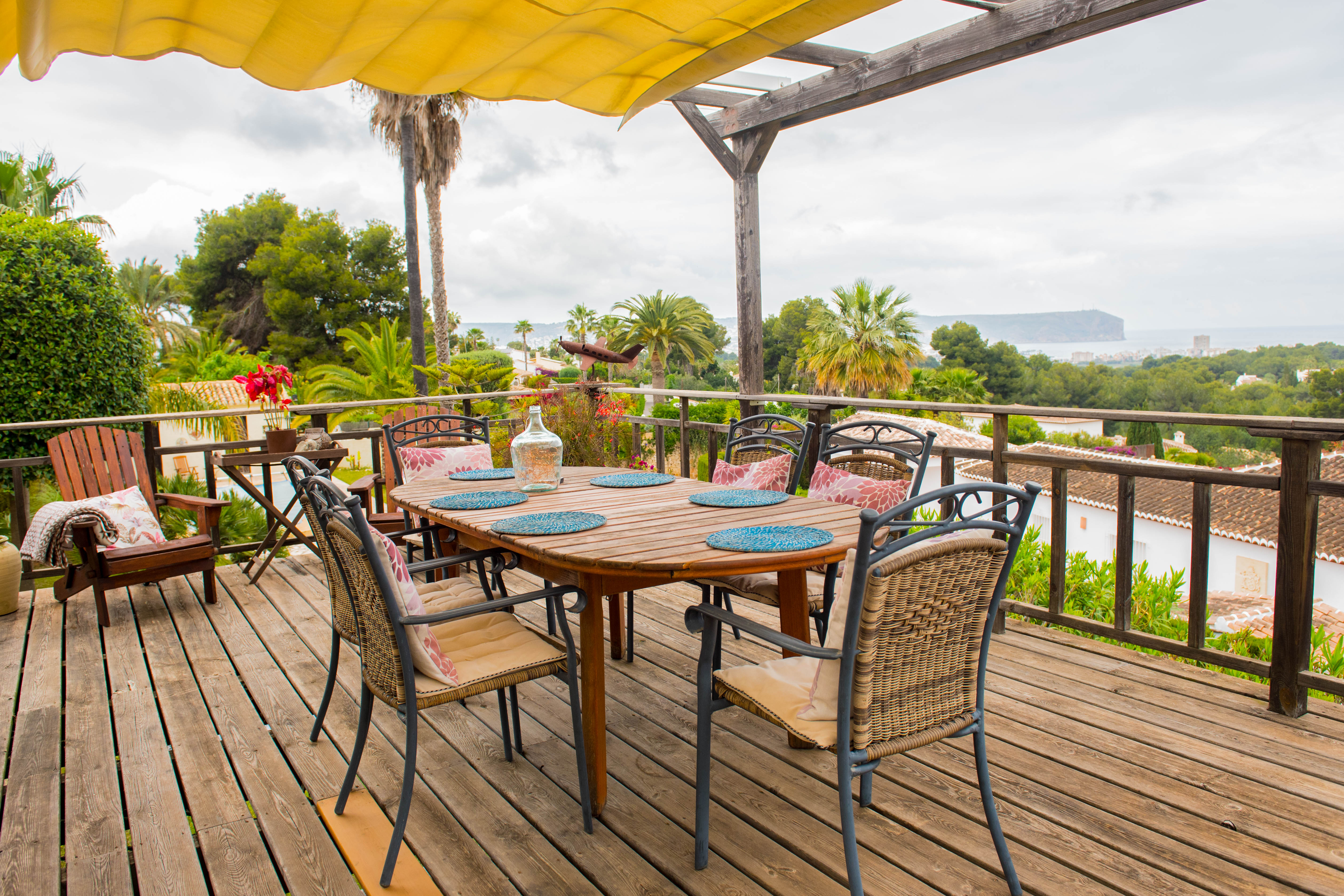 Holzterrasse mit gelber Gelenkarmmarkise, Essplatz im Freien und weitem Panoramablick auf die Küstenlandschaft und das Meer.