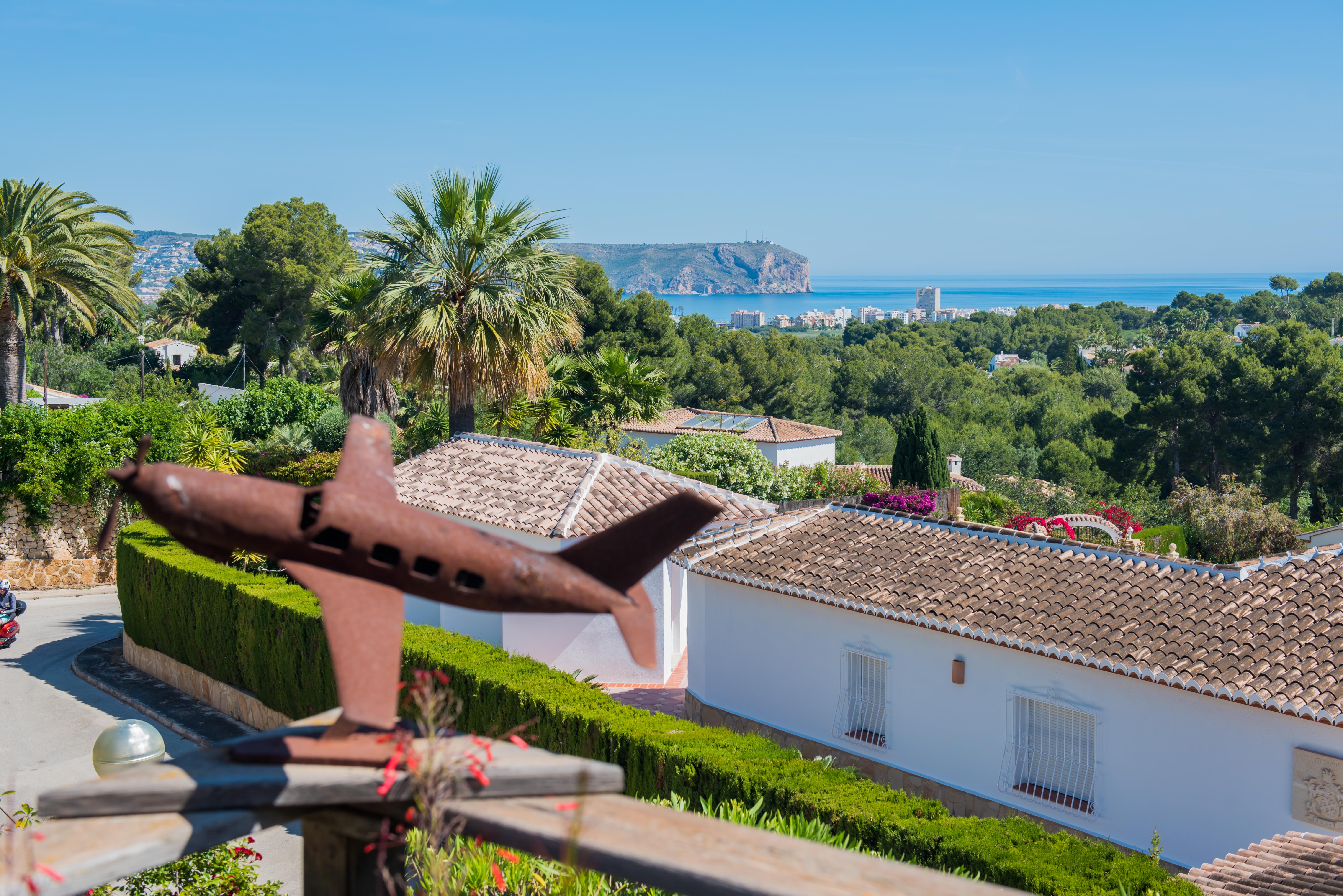 Panoramablick auf Jávea von der Terrasse, mit einer Flugzeugskulptur im Vordergrund und üppigem Grün.