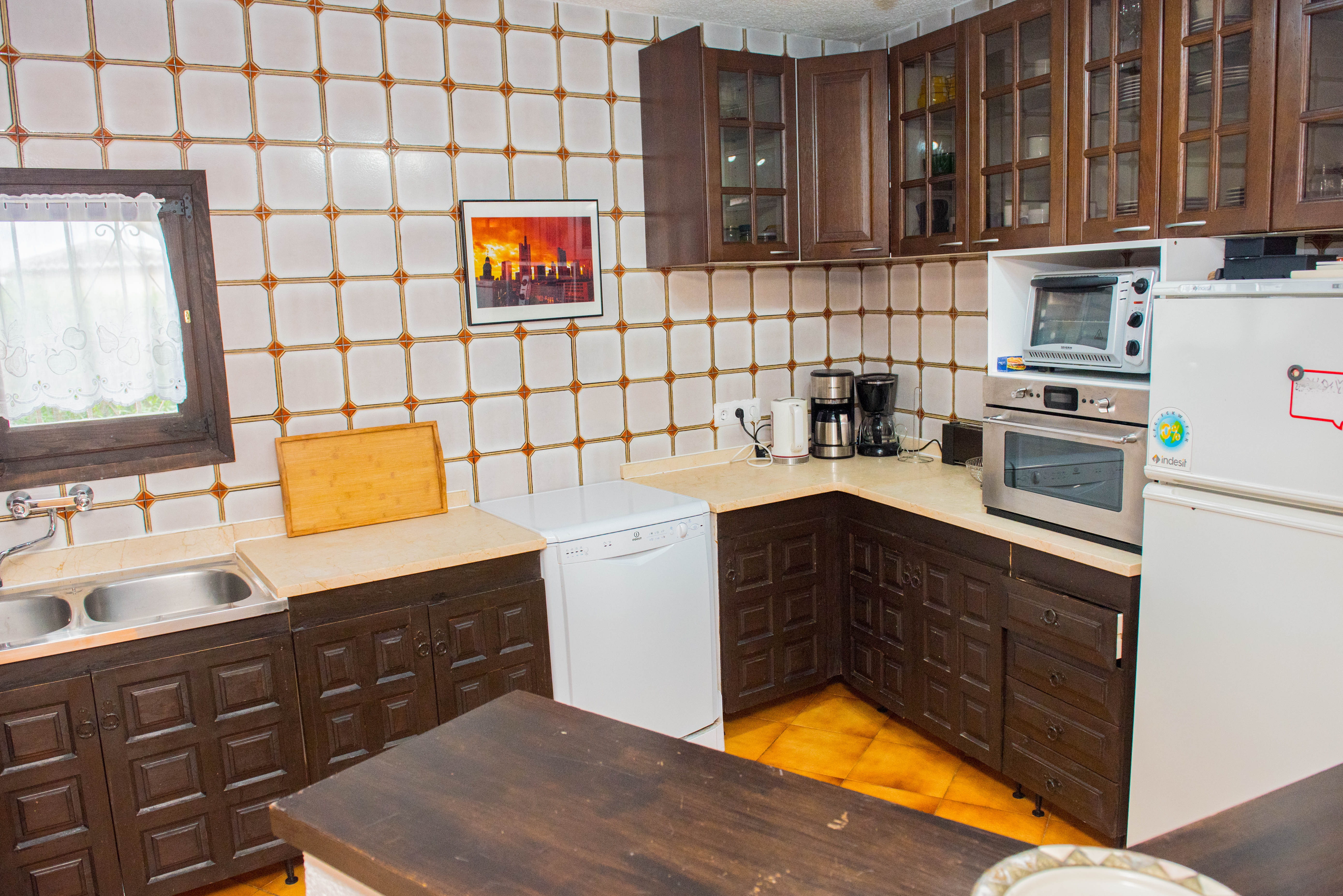 Rustikale Küche mit dunklen, geschnitzten Holzschränken, cremefarbener Arbeitsplatte und gemusterten Wandfliesen. Mit weißem Geschirrspüler und Einbaubackofen.
