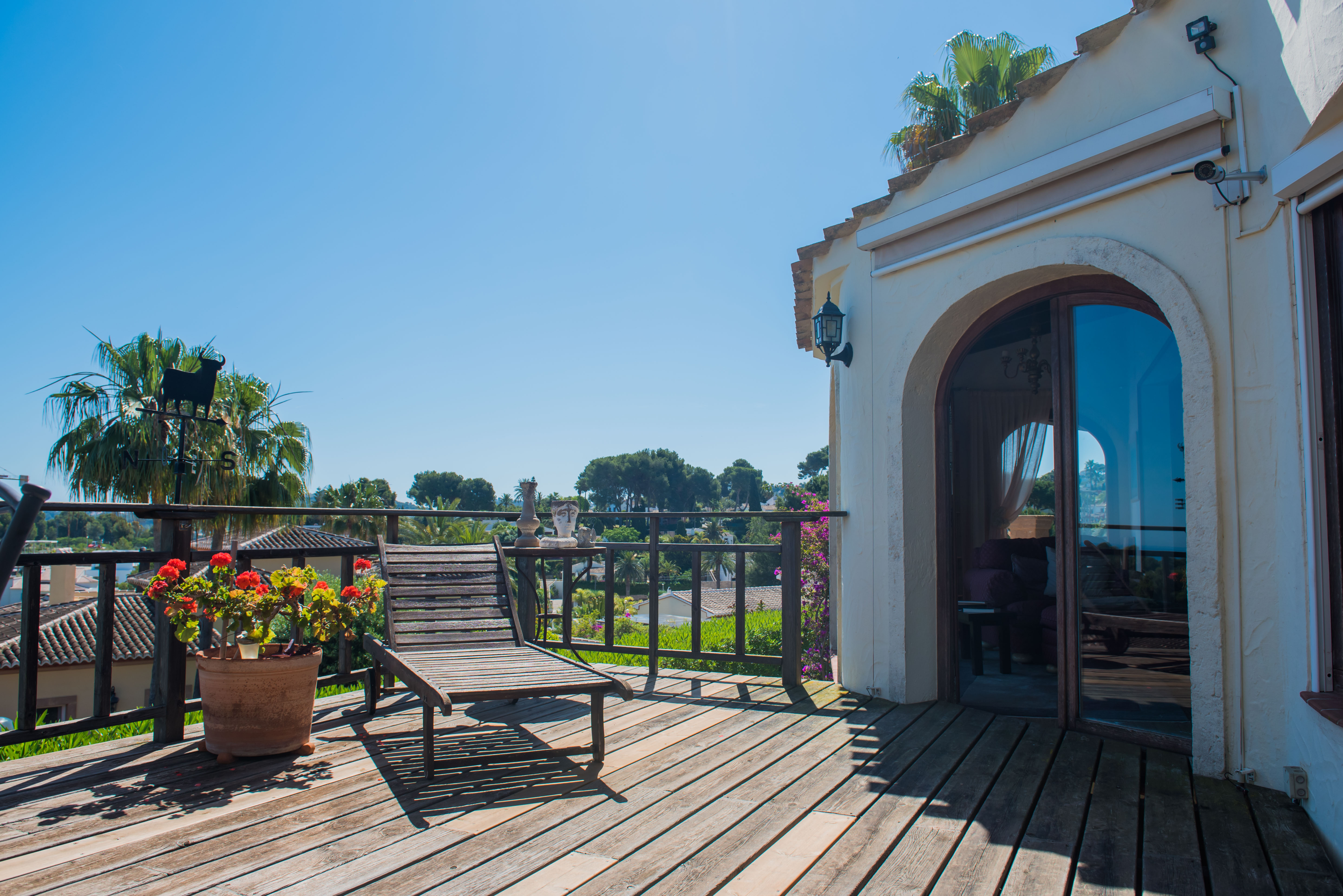 Sonnige Terrasse mit Holzboden, Liegestuhl und Blick auf die mediterrane Landschaft.