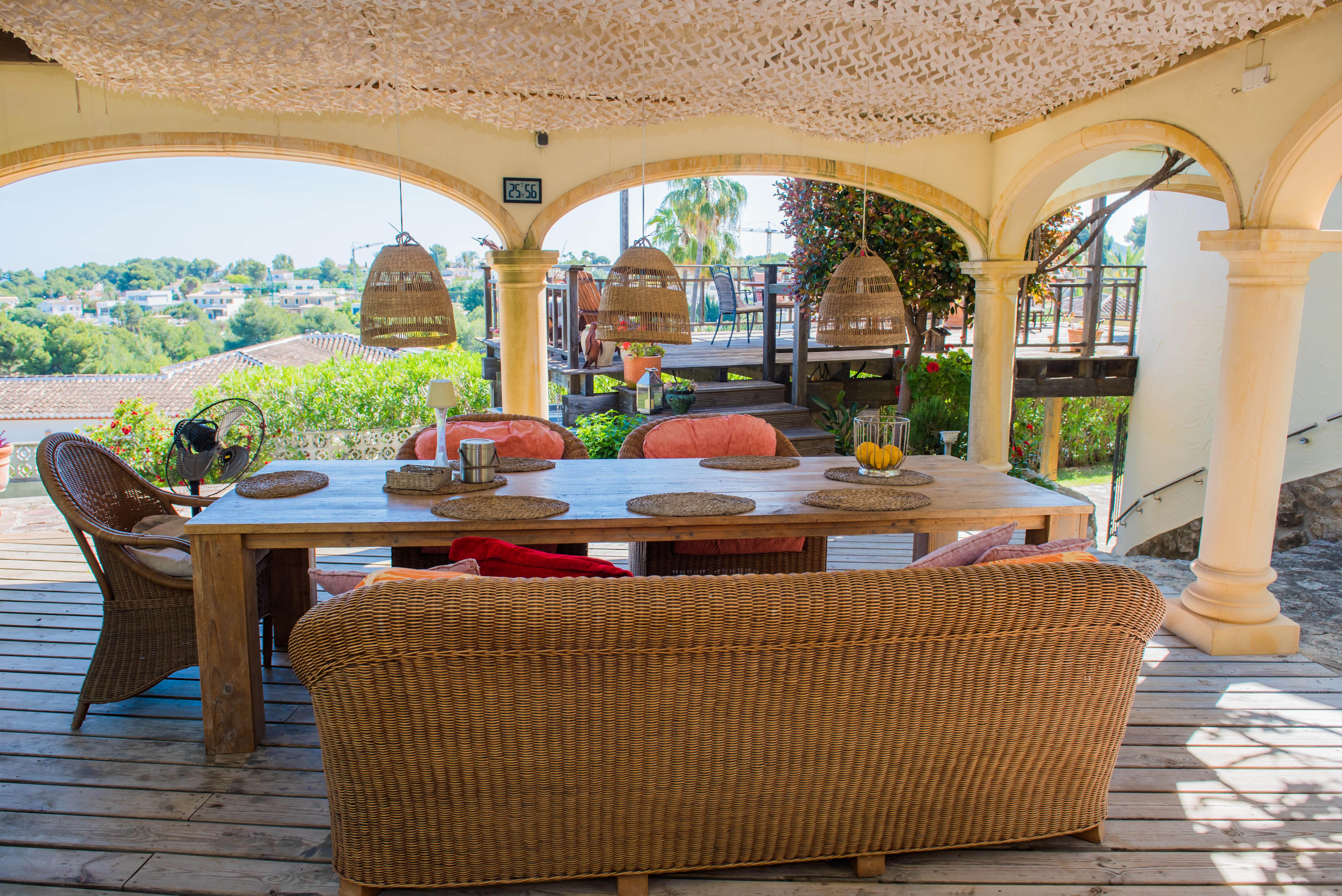 Veranda mit rustikalem Holztisch und Korbsesseln, beleuchtet mit Korblampen, mit Blick auf die Landschaft.