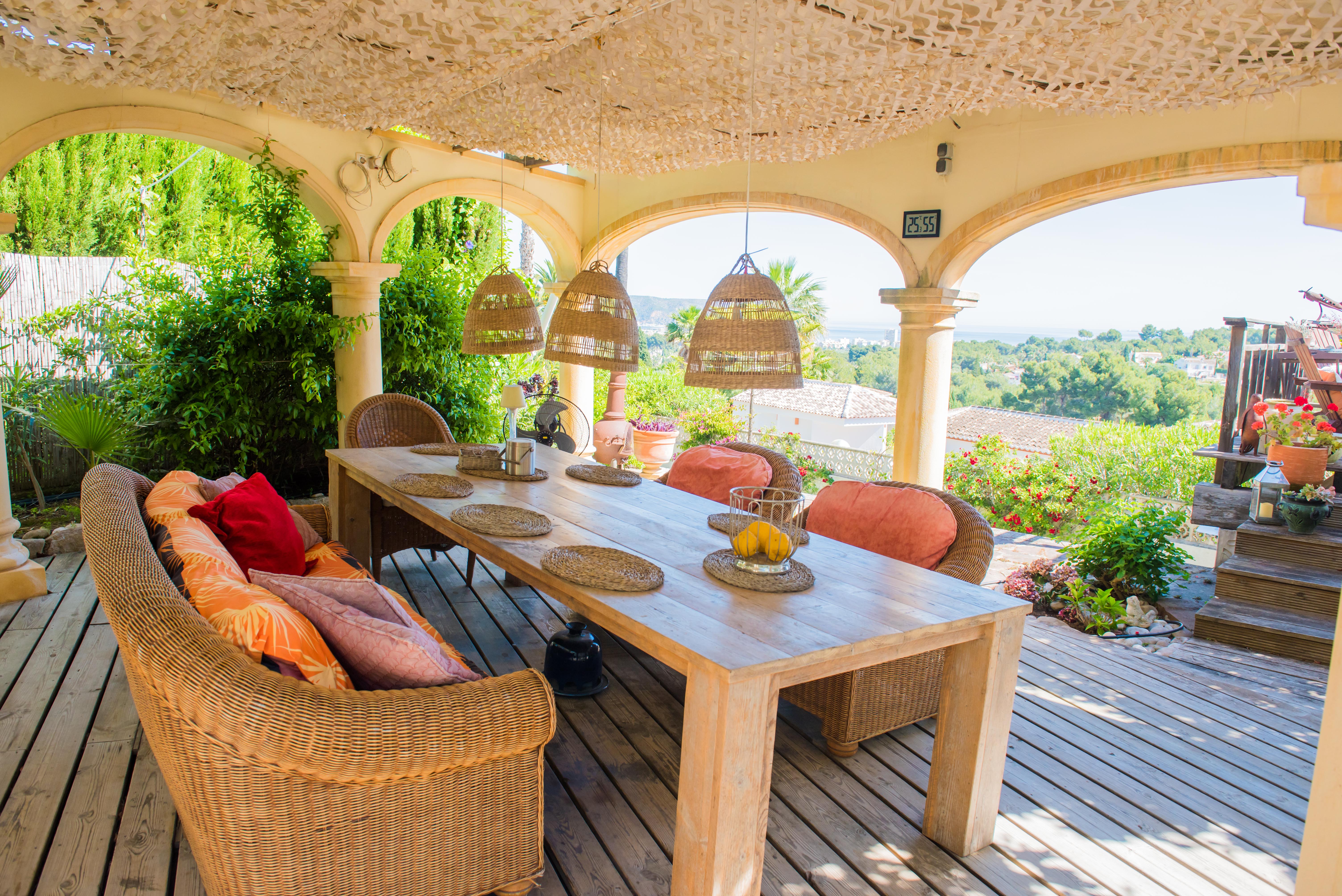 Veranda mit rustikalem Holztisch und Korbsesseln, mit Panoramablick auf den Garten und das Mittelmeer.