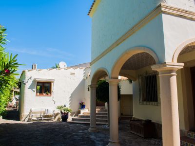 Außenansicht der Villa mit Steinbögen und weißen, strukturierten Wänden, umgeben von mediterranem Grün.