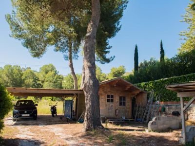 Blick auf den Holzschuppen und die überdachte Garage, umgeben von mediterraner Vegetation und klarem Himmel.