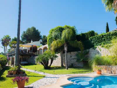 Gartenansicht mit blauem Mosaikpool und Steinpfad, der zur Villa im mediterranen Stil führt.