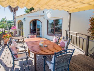 Überdachte Terrasse mit Holztisch und gepolsterten Stühlen, ideal, um den Panoramablick auf das Mittelmeer zu genießen.