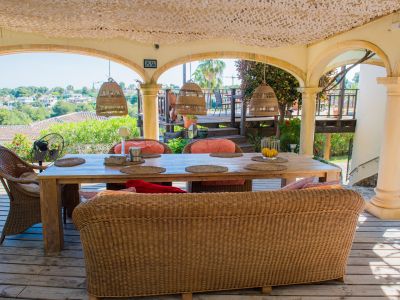 Veranda mit rustikalem Holztisch und Korbsesseln, beleuchtet mit Korblampen, mit Blick auf die Landschaft.