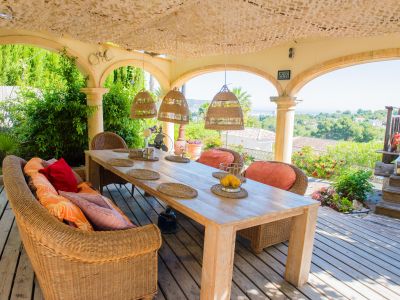 Veranda mit rustikalem Holztisch und Korbsesseln, mit Panoramablick auf den Garten und das Mittelmeer.