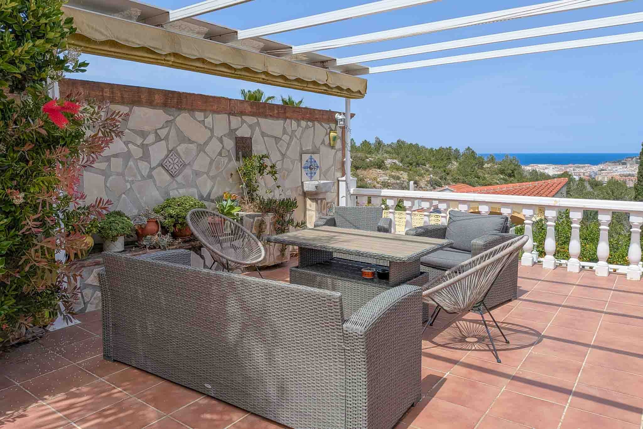 Außenterrasse mit Rattan-Sitzgruppe, Terrakottaboden und Panoramablick auf das Meer. Mit Pergola, ausziehbarer Markise und dekorativer Natursteinwand.