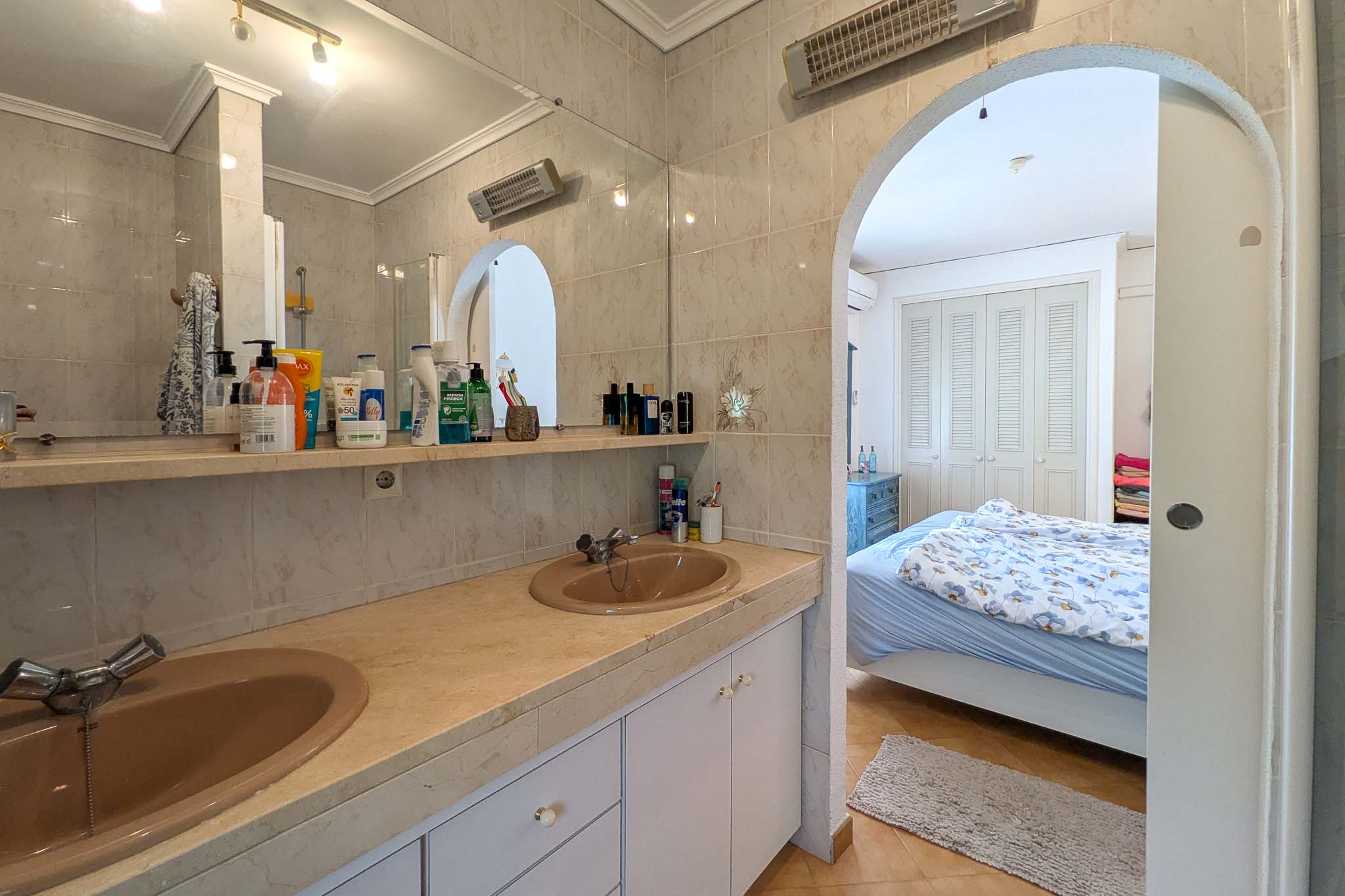 En-Suite-Badezimmer mit Doppelwaschbecken auf Marmorplatte, durch einen Rundbogen direkt mit dem Schlafzimmer verbunden.