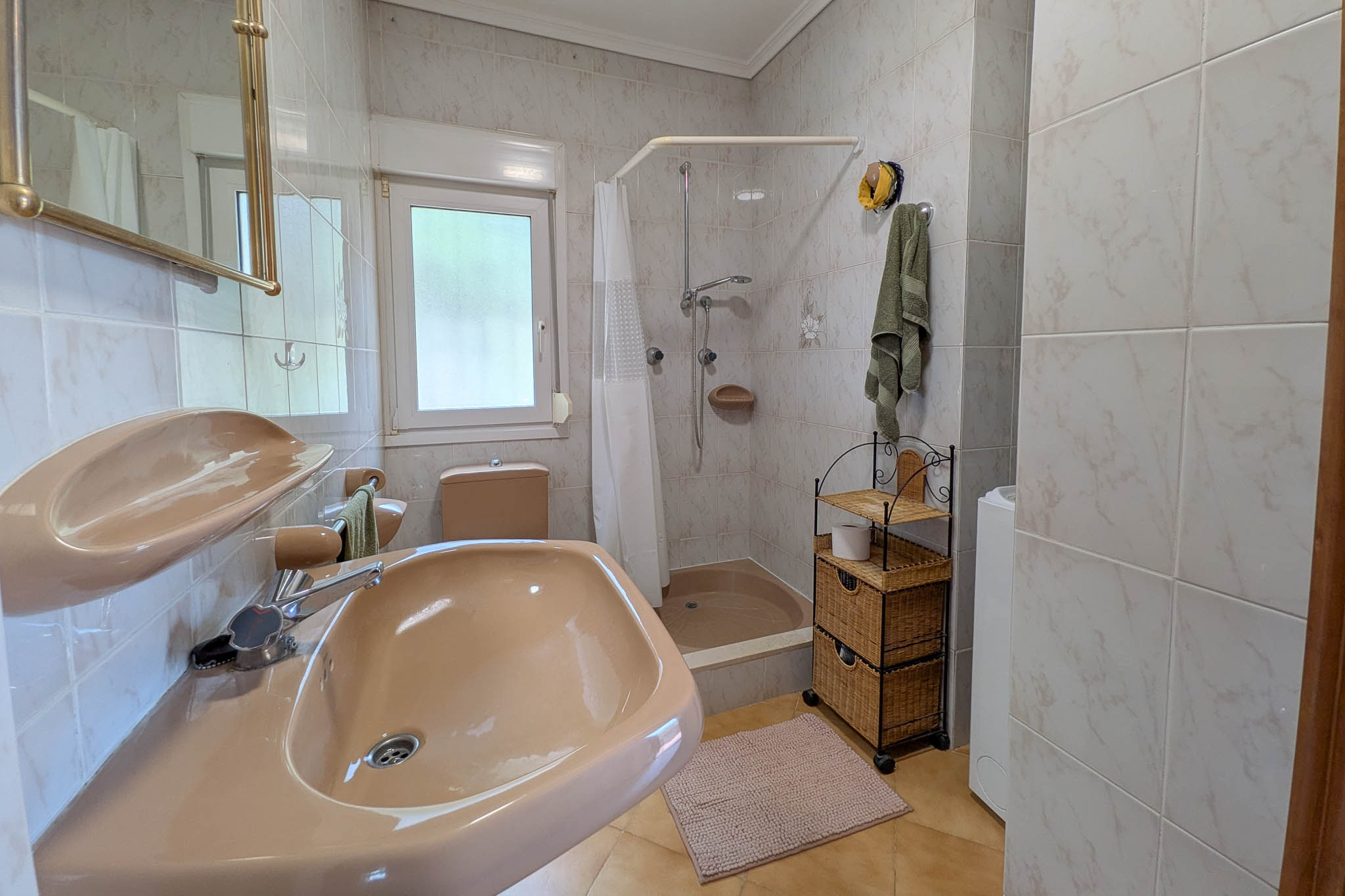 Funktionelles Badezimmer mit lachsfarbener Keramik, Duschwanne mit Vorhang, gefliesten Wänden und Fenster für natürliche Belüftung.