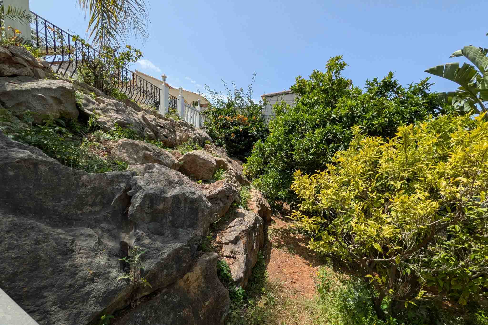 Kaskadierender Garten mit natürlichen Felsformationen, Erdwegen und mediterranen Zitrusbäumen am Hang von La Pedrera.