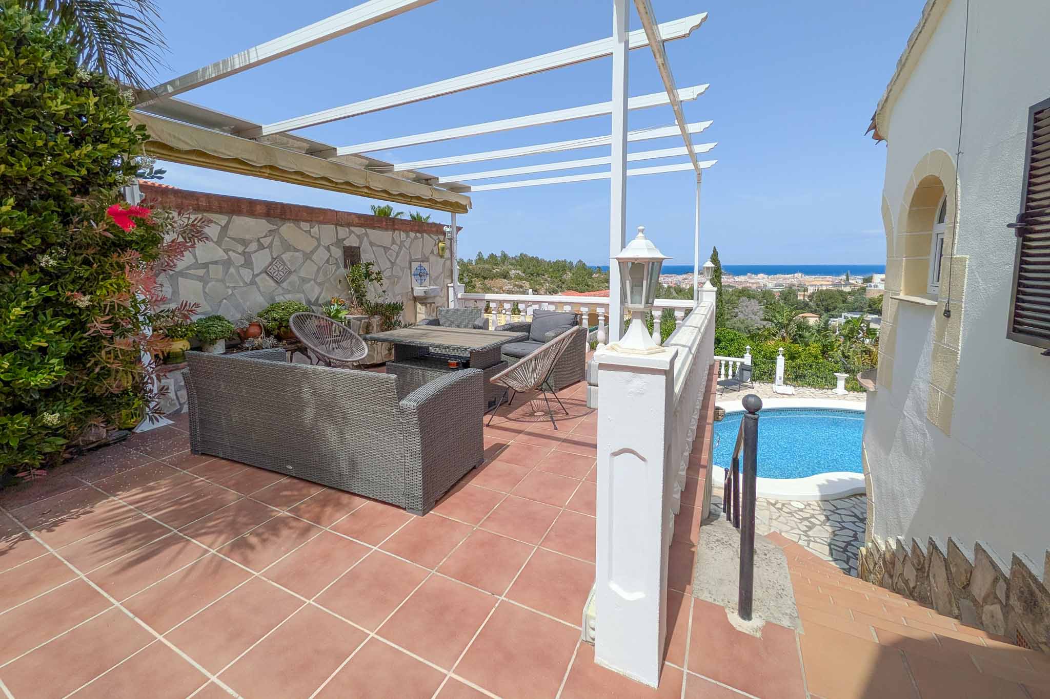 Obere Terrasse mit Außenlounge, weißer Pergola und Panoramablick auf das Mittelmeer und Dénia, mit Blick auf den darunter liegenden Poolbereich.