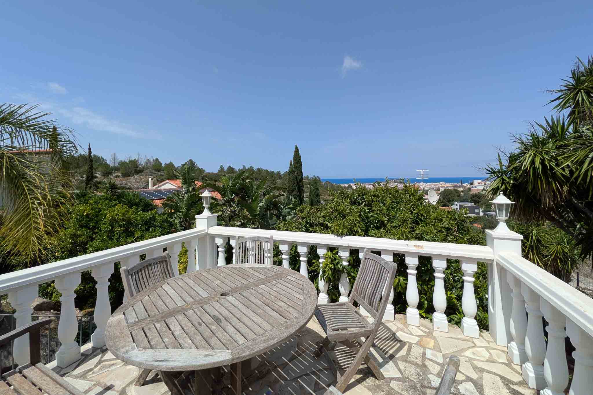 Terrasse mit weißer Balustrade und Holzmöbeln auf Natursteinboden, mit weitem Blick auf das Mittelmeer und das Stadtgebiet von Dénia.