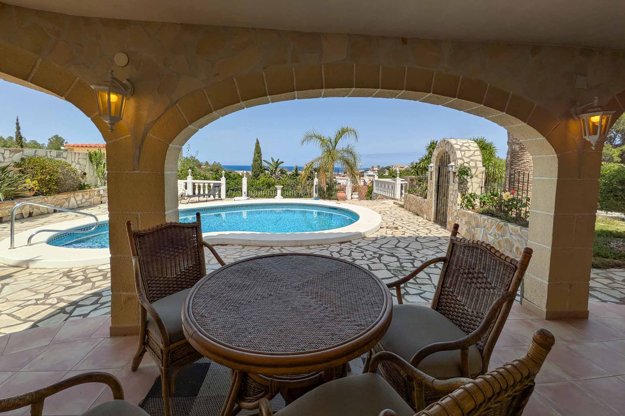 Überdachte Terrasse mit Natursteinbögen und Rattanmöbeln, mit Blick auf den privaten Pool und das ferne Mittelmeer.