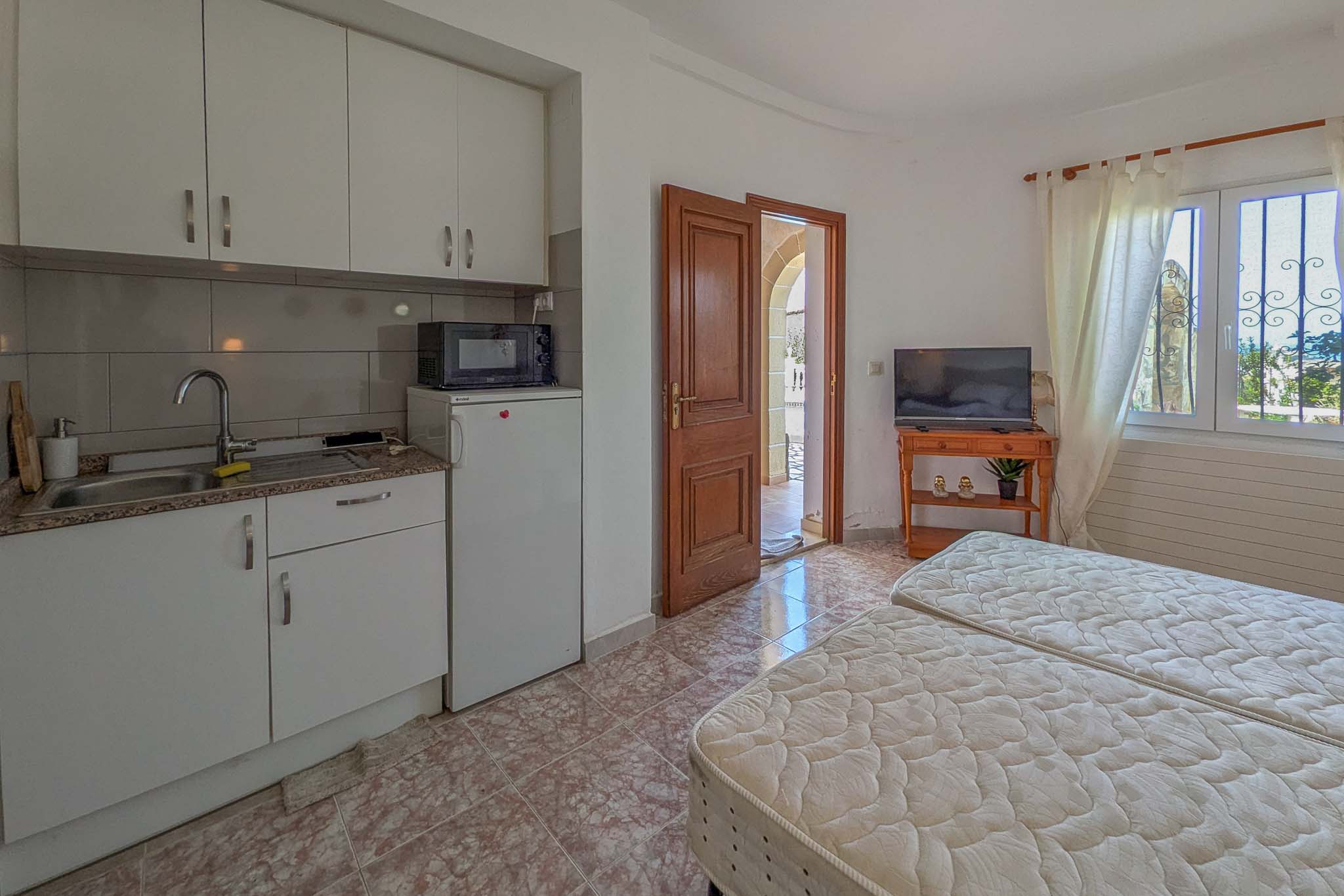 Unabhängiges Apartment im Erdgeschoss mit integrierter Küchenzeile, zwei Einzelbetten und direktem Zugang zum Außenbereich durch eine Holztür.