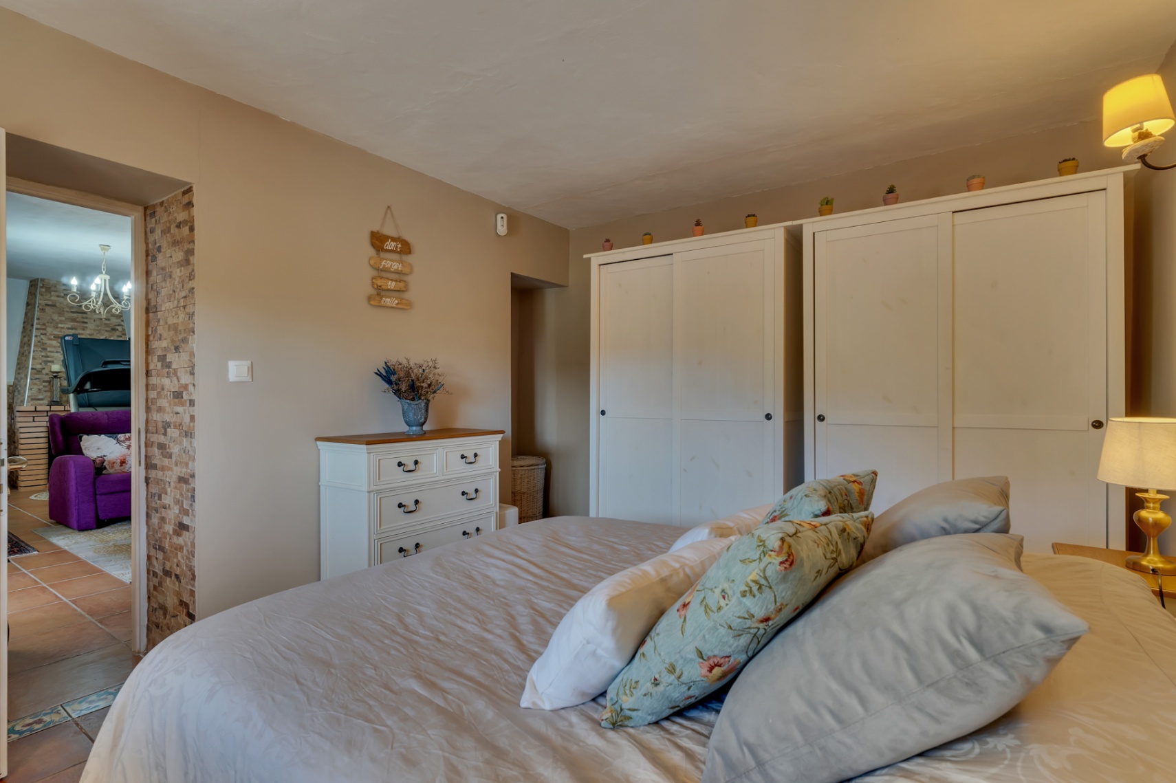 Gemütliches Schlafzimmer mit weißen Schiebetürenschränken, klassischer Kommode und einer Natursteinwand am Durchgang zum Wohnbereich.