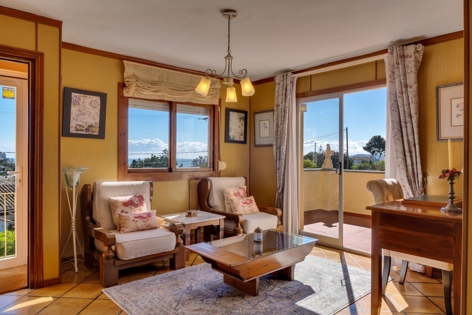 Heller Wohnbereich mit Holzsesseln, Glastisch und direktem Zugang zur Terrasse mit Panoramablick auf das Mittelmeer.