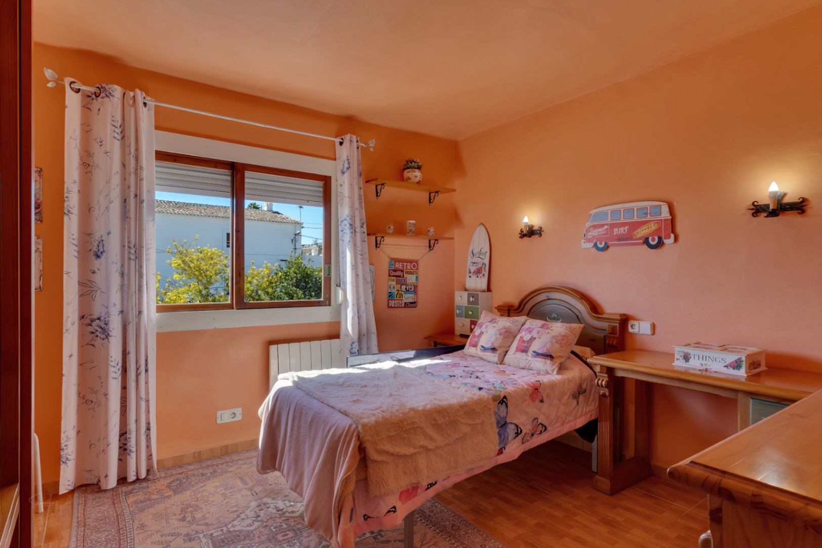 Helles Schlafzimmer mit pfirsichfarbenen Wänden, Massivholzmöbeln, Schreibtisch und Fenster. Inklusive Wandheizkörper und klassischem Fliesenboden.