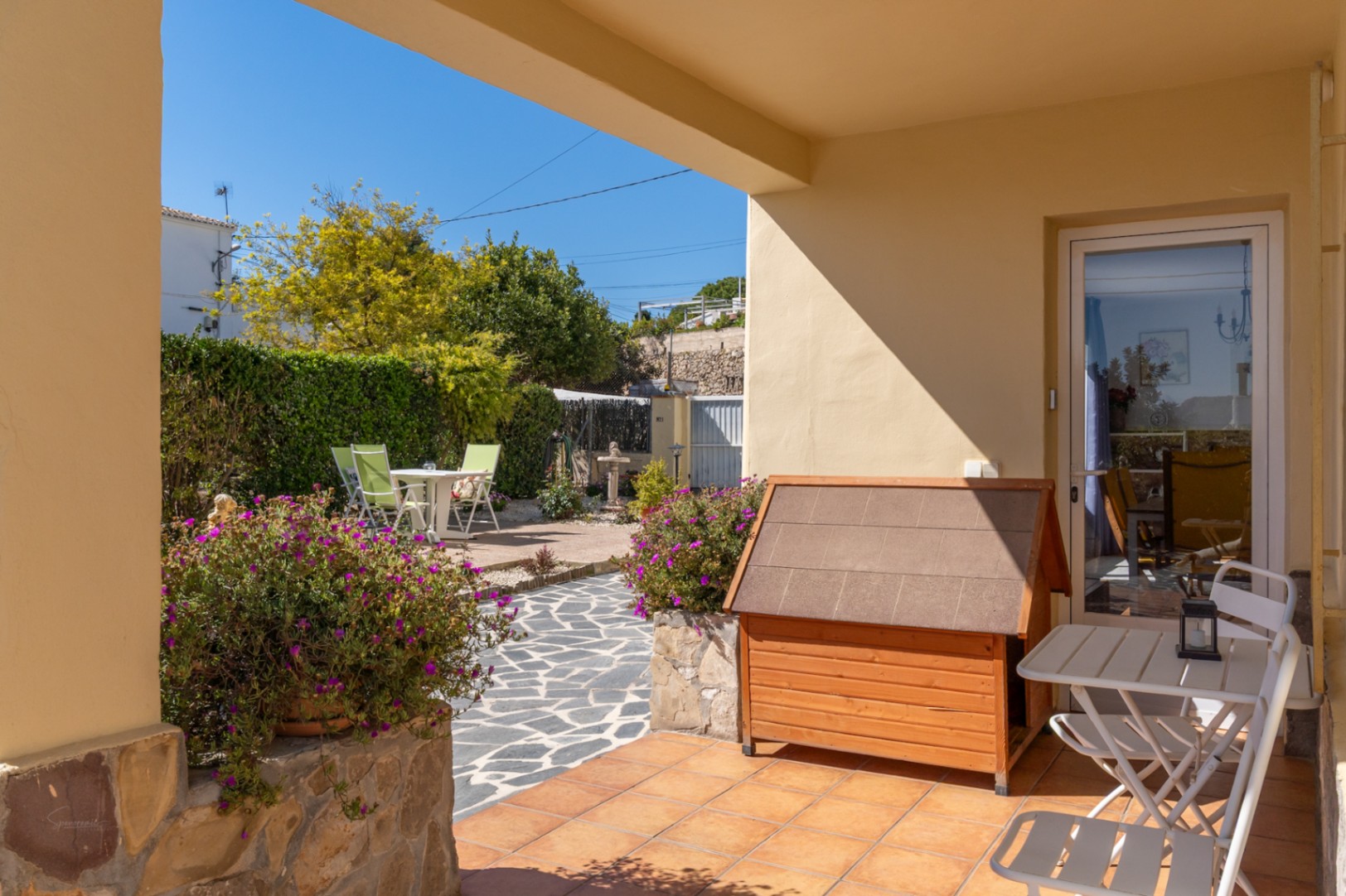Überdachte Terrasse mit Terrakottaboden, Gartenmöbeln und Blick auf den gepflegten Garten mit Natursteinpflaster.