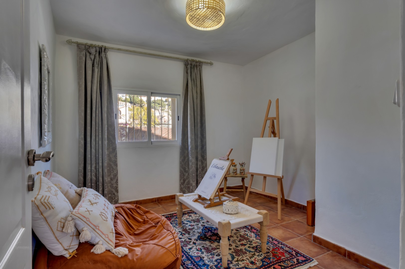 Vielseitiges Zimmer mit Terrakottaboden, eingerichtet als Kunstatelier mit Holzstaffelei, natürlichem Licht und gemütlicher Sitzecke.