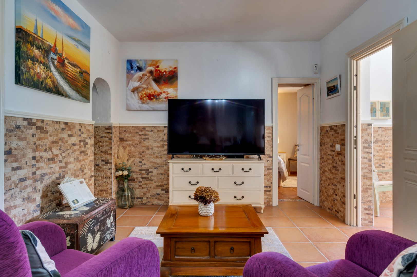 Wohnbereich mit Steinoptik-Wandsockel, Terrakottaböden und rustikalen Möbeln, der die Schlafzimmer im Erdgeschoss miteinander verbindet.