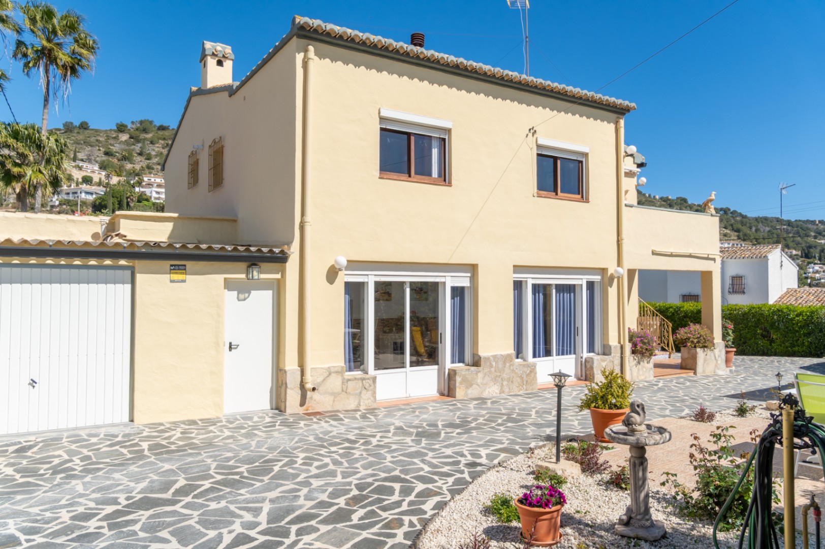 Zweistöckige Villa mit Steinsockel, großen Glasfronten im Erdgeschoss und einer weitläufigen Terrasse mit Natursteinpflasterung.