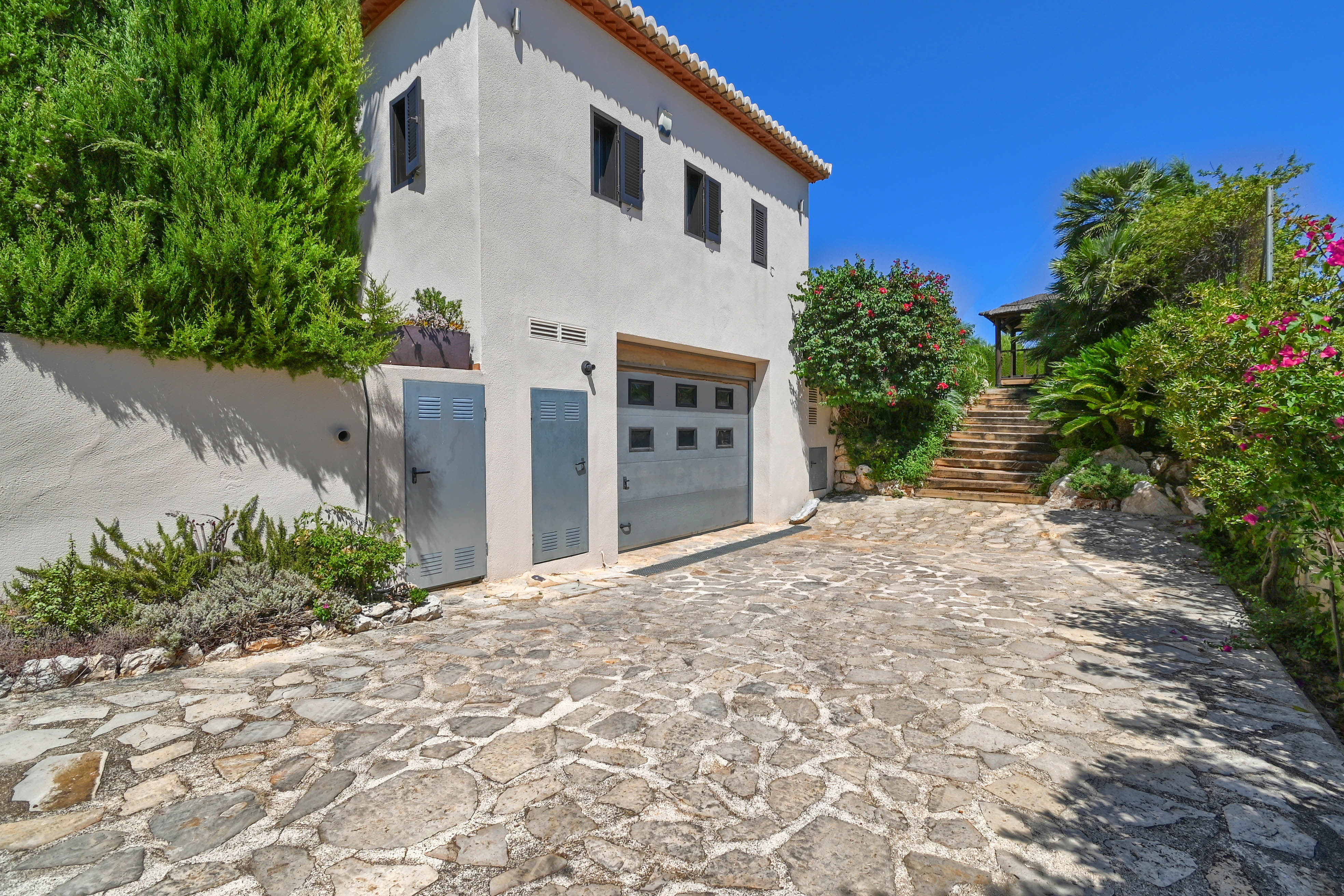 Außenansicht der Villa mit Steinfahrt, Grün und grauer Garage.