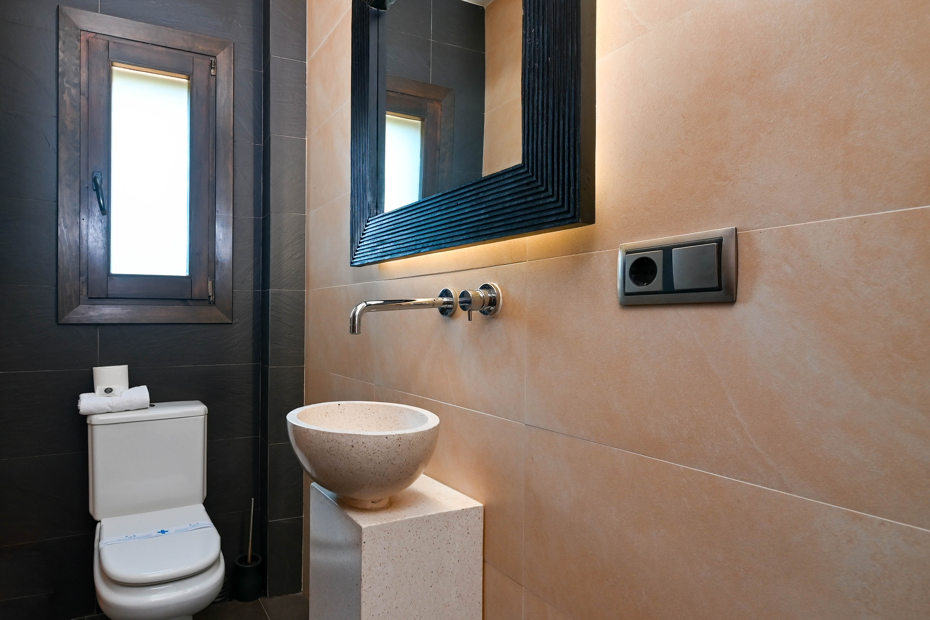 Badezimmerdetail mit Steinwaschbecken auf Sockel und Spiegel mit integrierter Beleuchtung.