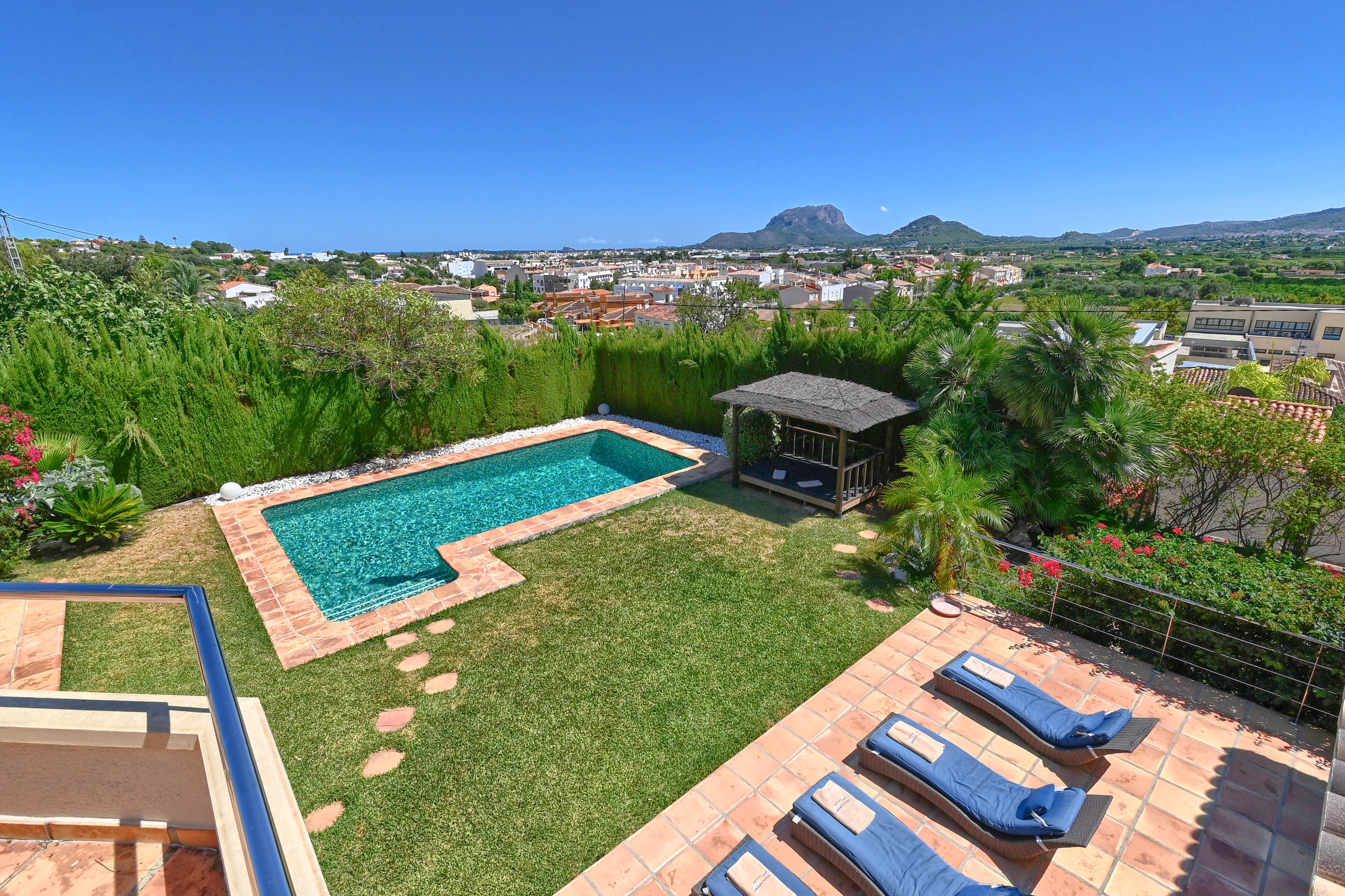 Erhöhte Ansicht des Gartens mit türkisfarbenem Pool und strohgedecktem Pavillon.