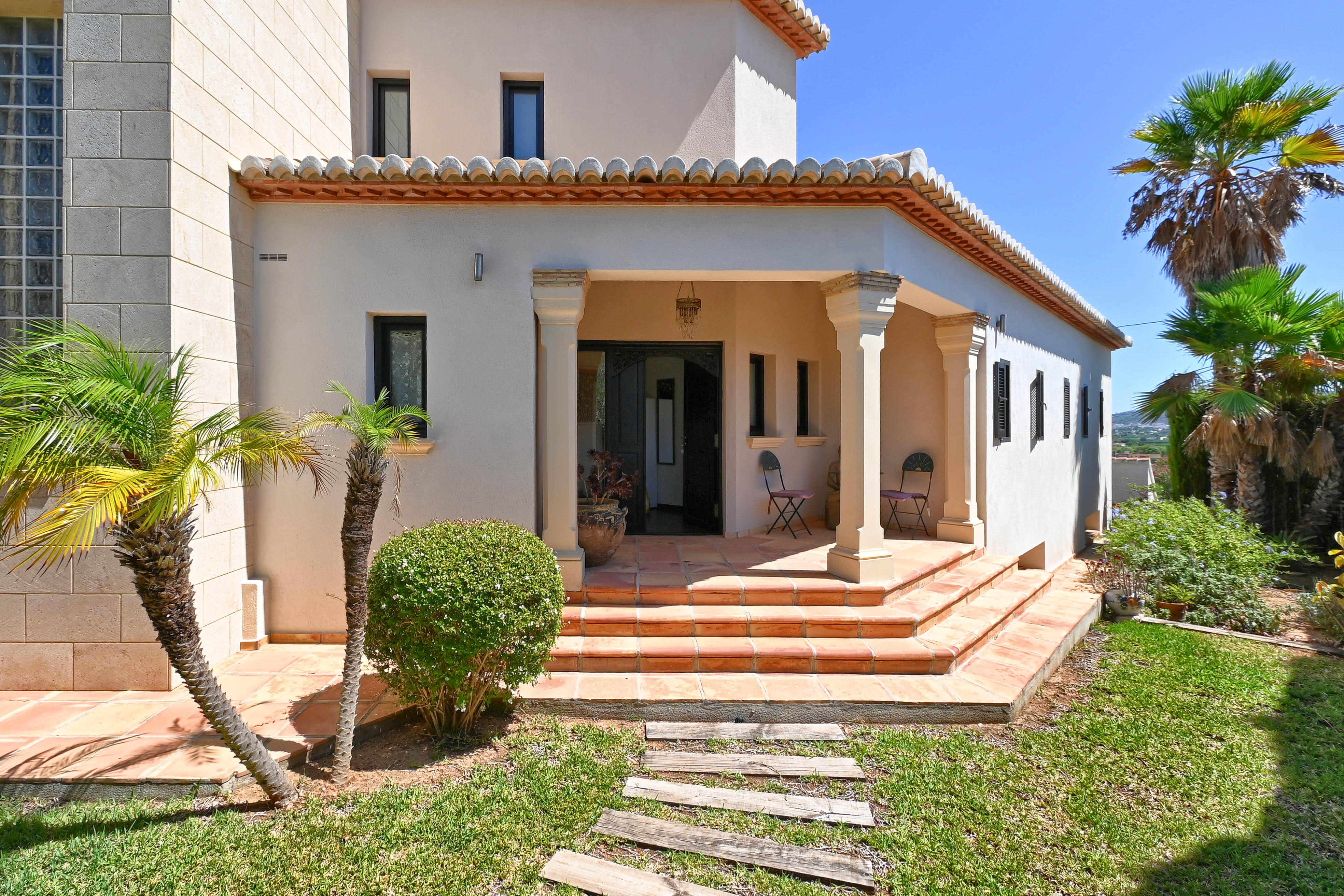 Haupteingang der Villa mit Terrakotta-Stufen und gepflegtem Garten mit Palmen.