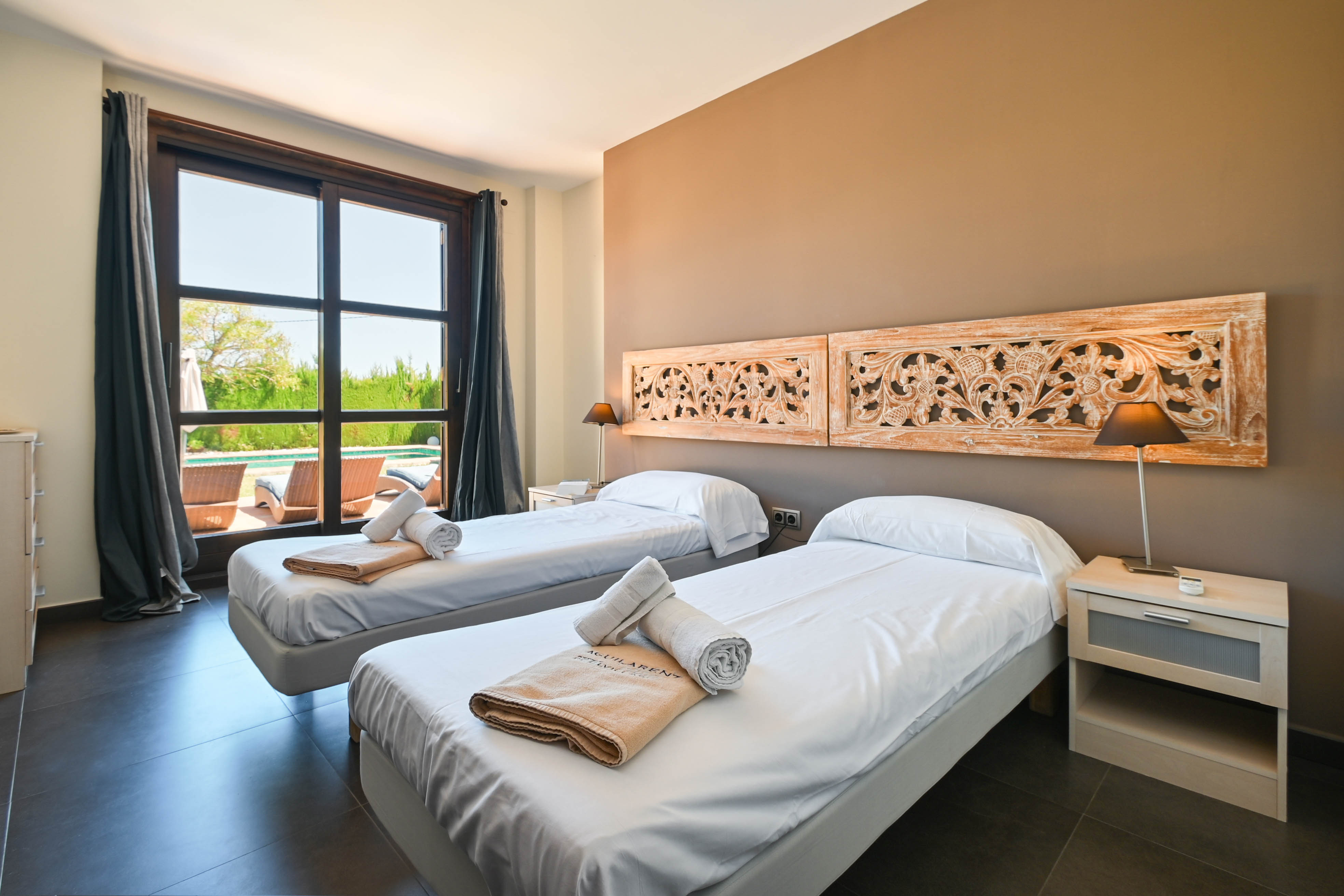 Helles Schlafzimmer mit Einzelbetten, geschnitzten Holz Kopfteilen und Blick auf den Pool.