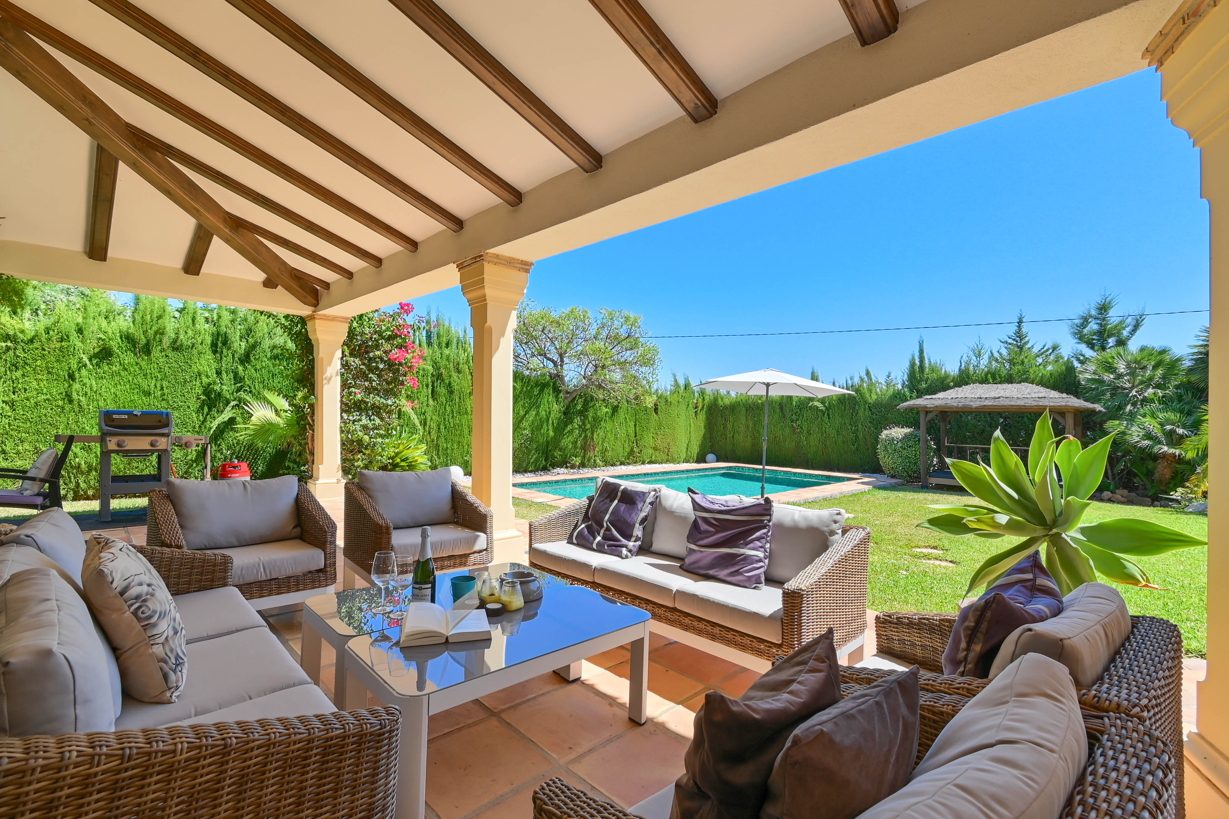 Möblierte Veranda mit Korbmöbeln mit Blick auf Pool und Garten.