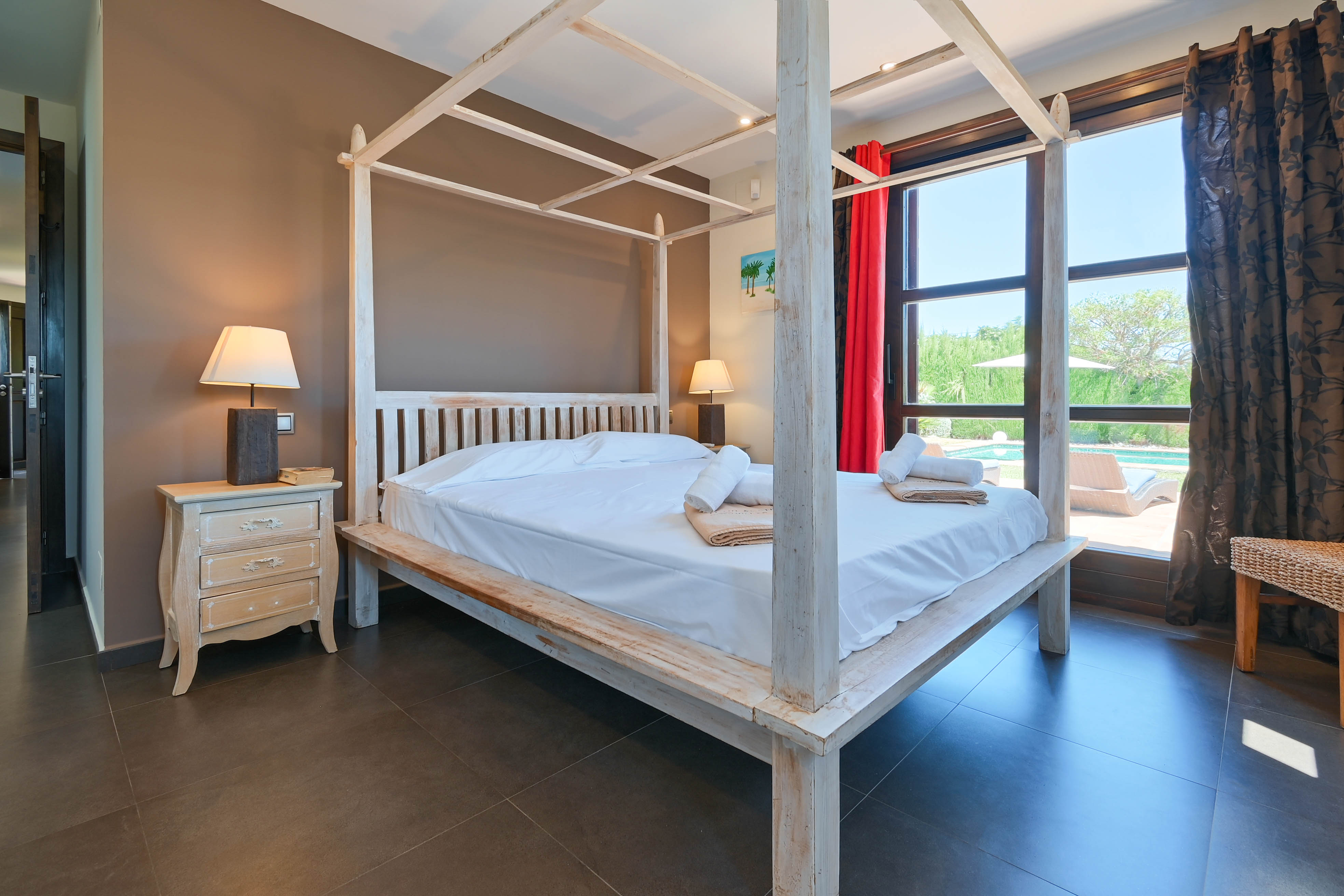 Schlafzimmer mit weißem Holzhimmelbett, Nachttisch im Used-Look und Blick auf den Pool.