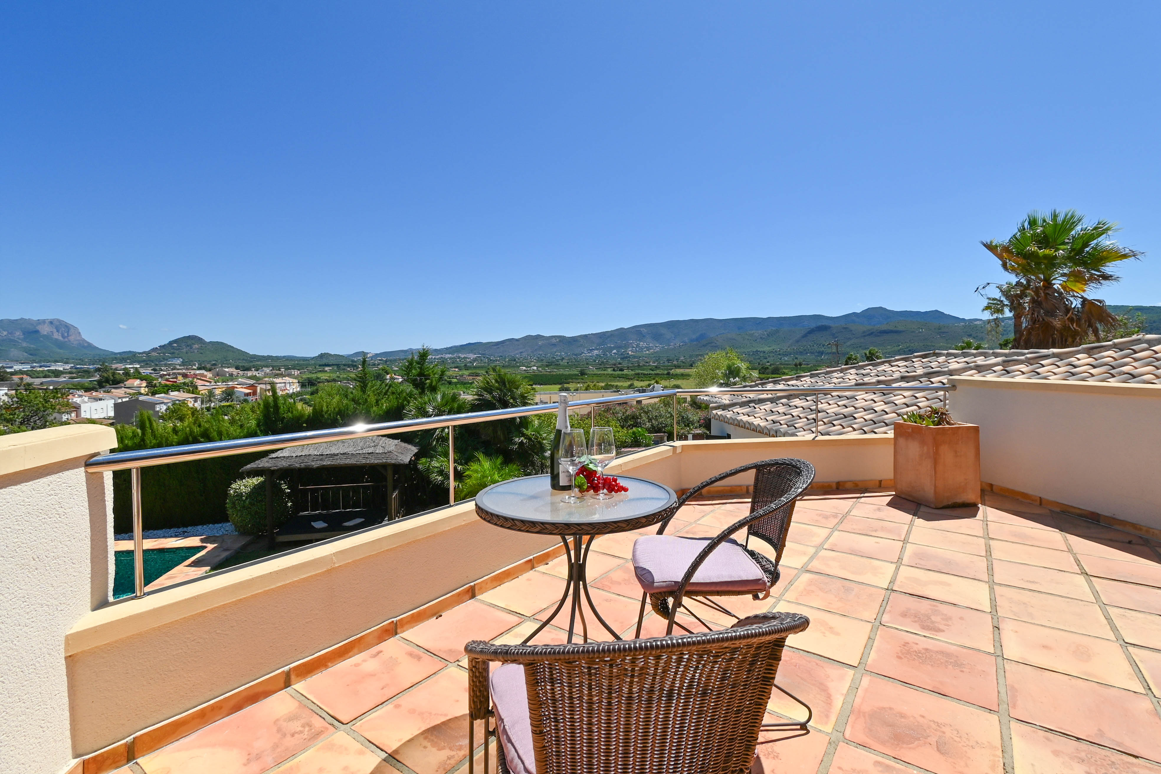 Terrasse mit Glastisch, Korbstühlen und Blick auf das Tal und die Berge.
