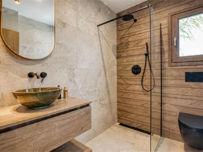 Badezimmerdetail mit Steinwaschbecken auf Holzplatte und Glasdusche.